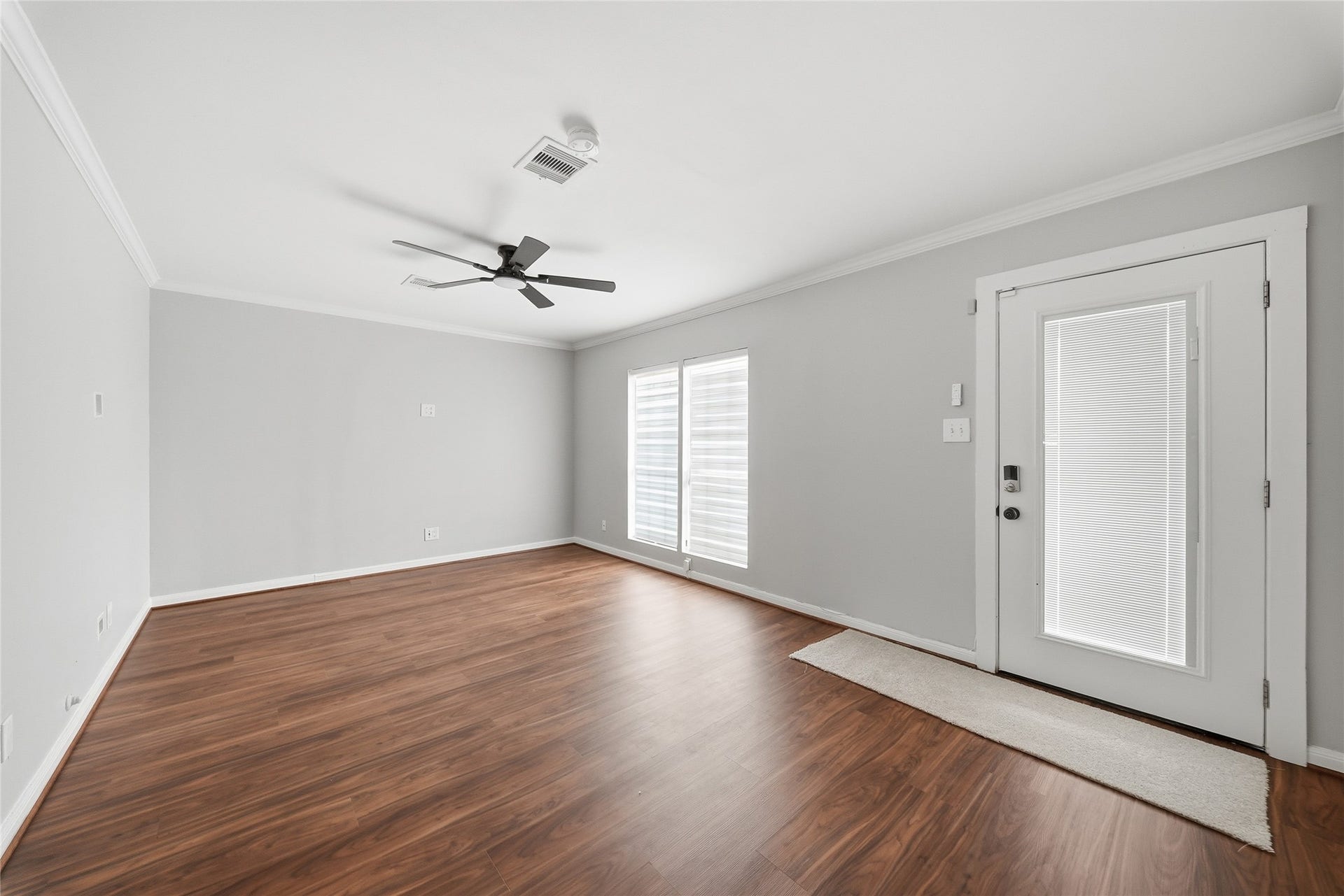 Bright and inviting room featuring sleek new flooring, neutral gray walls, and ample natural light through large windows, complemented by a modern ceiling fan.