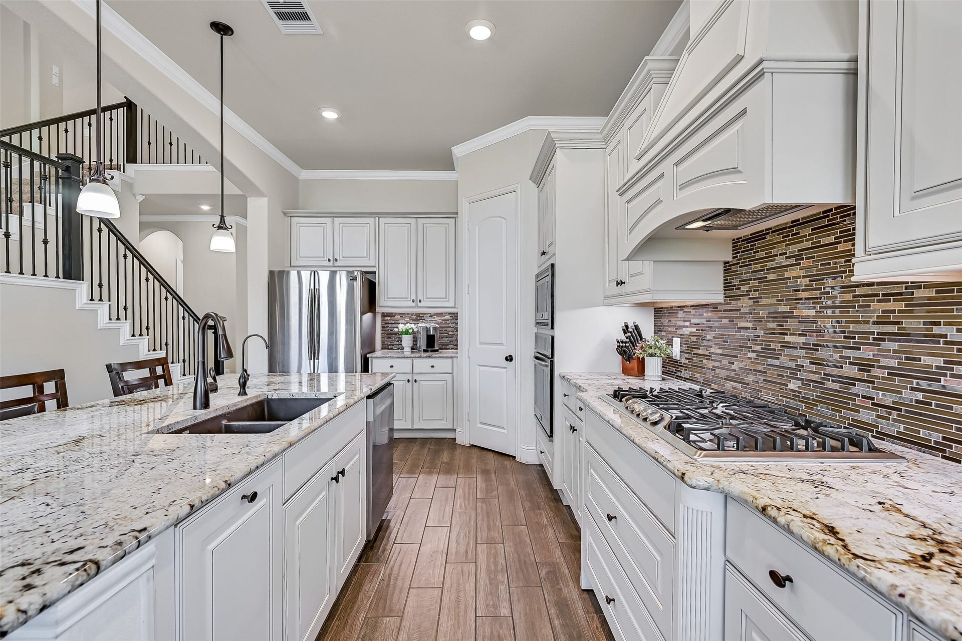 1645 Longwood Glen Lane, Friendswood, TX 77546 This angle highlights the kitchens well-planned workspace, with generous granite prep surfaces, a dual-basin composite sink with revere osmosis water filtration, a five-burner gas cooktop, built-in oven and microwave, and a corner walk-in pantry. Abundant cabinetry keeps everything organized.