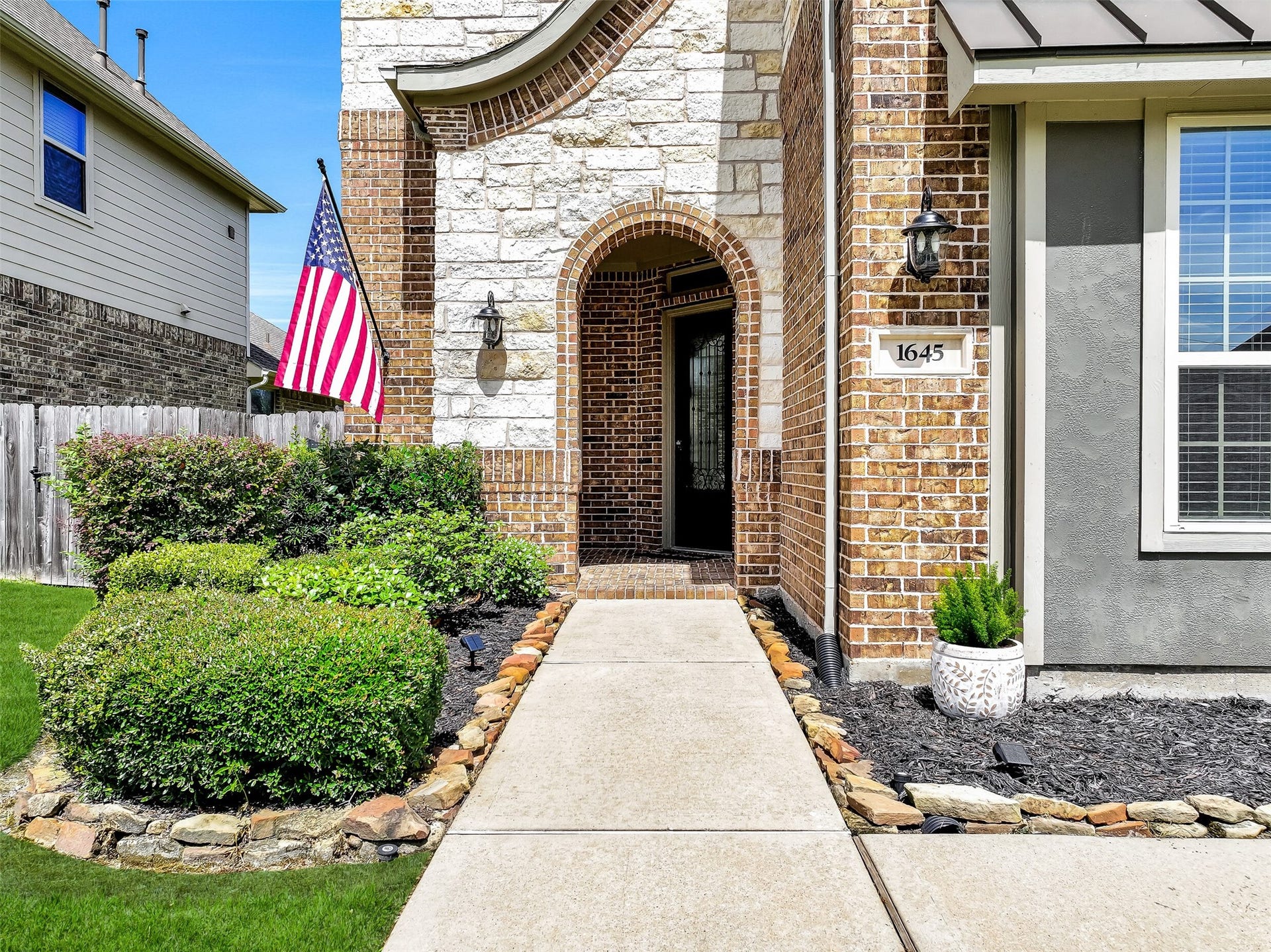 1645 Longwood Glen Lane, Friendswood, TX 77546 A covered front porch and impressive 8-foot mahogany entry door with pleated glass and wrought iron detailing create a warm welcome for guests. Stone landscape borders, fresh mulch, and mature landscaping enhance the inviting approach to this exceptional home.
