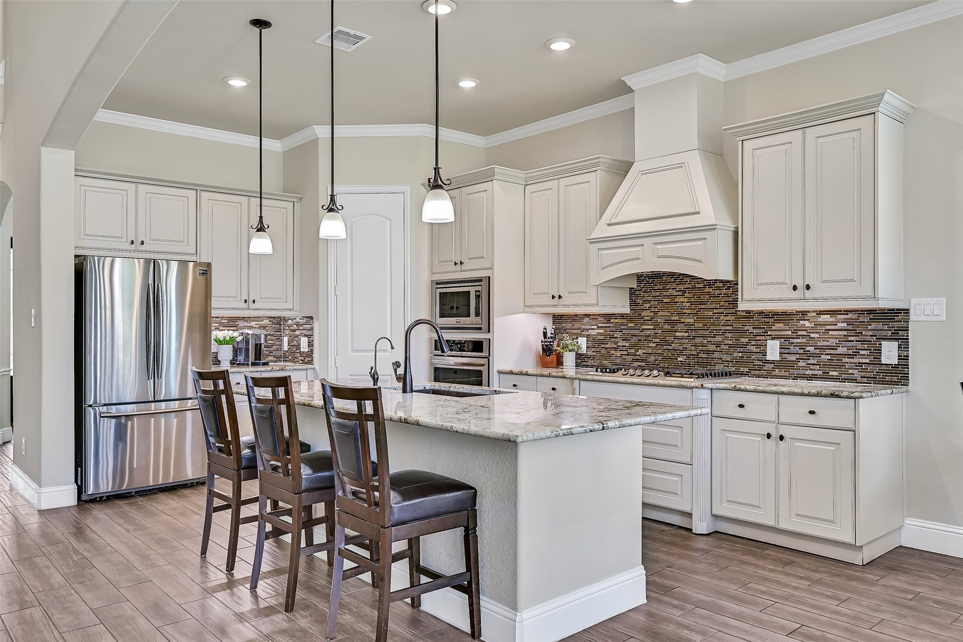 1645 Longwood Glen Lane, Friendswood, TX 77546 Designed with both style and functionality in mind, the kitchen features granite countertops, a five-burner gas cooktop, built-in oven and microwave, a walk-in corner pantry, and an oversized island with a composite sink, oil-rubbed bronze fixtures, and integrated water filtrationperfect for preparing meals while staying connected to family and guests.