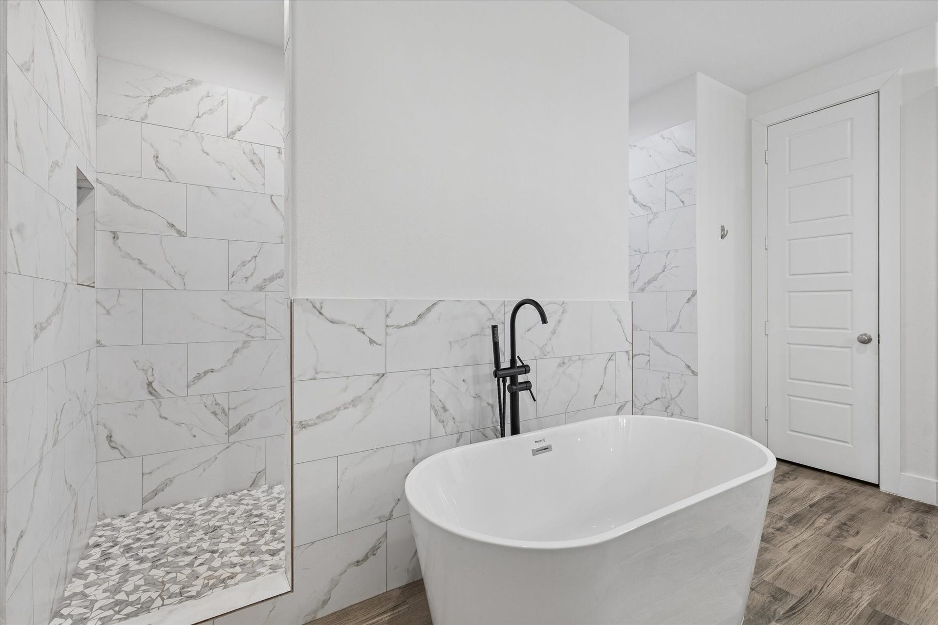 The elegant and modern bathtub is perfect for relaxing and recharging after a long day. The space showcases sophisticated design details, including wall tile colors that harmonize beautifully with the marble surfaces. The black faucet on the tub provides a striking contrast to the light color palette, while the spacious shower behind the tub and the attention to flooring details complete this unique and visually stunning bathroom. The surfaces are also easy to clean, combining style with functionality.