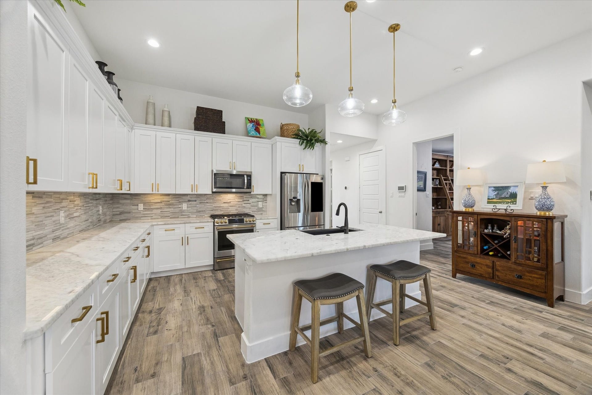This view highlights the marble countertops, elegant backsplash, and the kitchen island with space for stools, perfect for enjoying conversation with guests while entertaining. The thoughtful layout and placement of elements in this space create a functional yet sophisticated environment, making the kitchen as stylish as it is inviting.