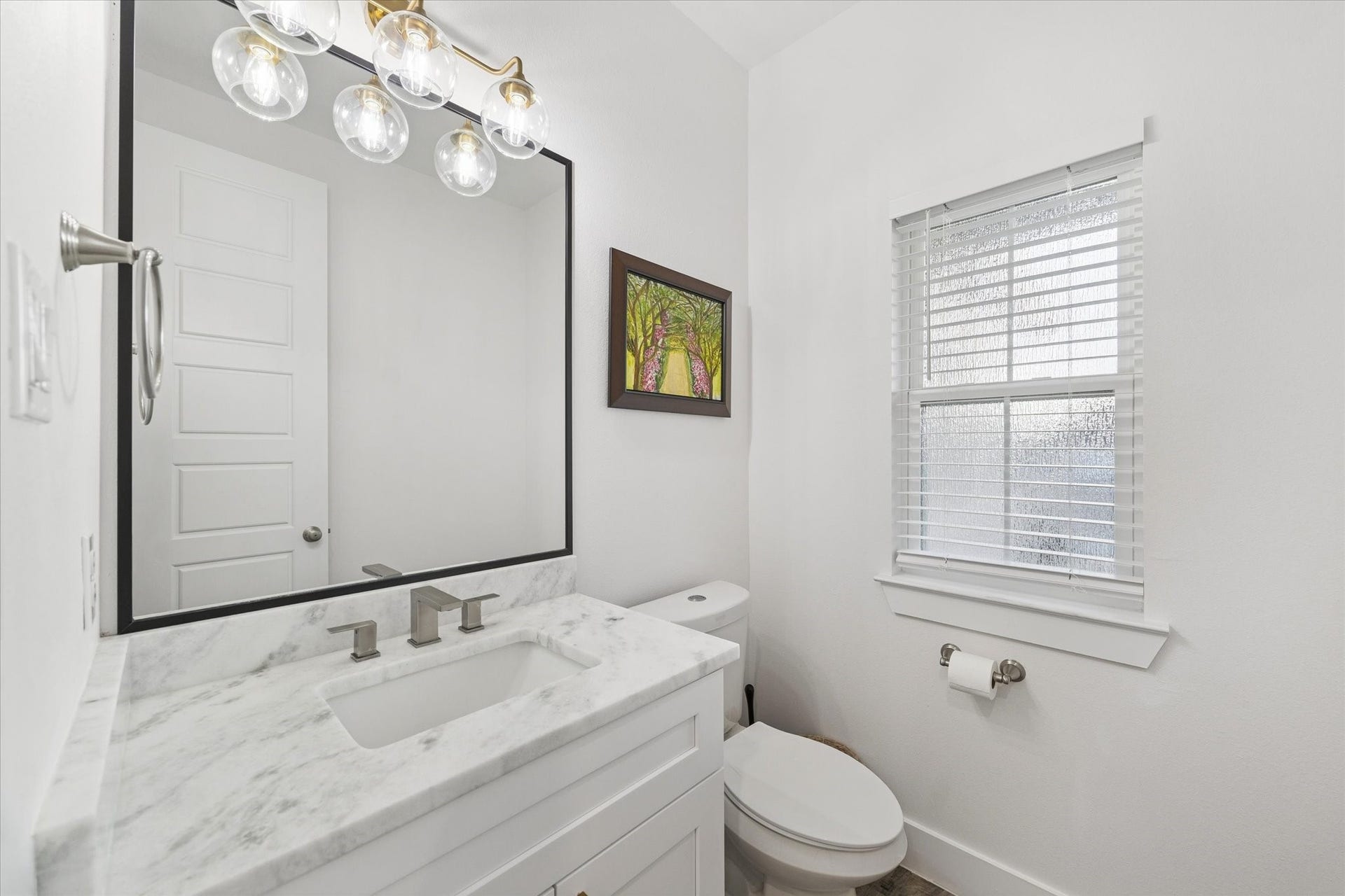 This powder room features refined details, including a marble countertop, high-efficiency toilet, and custom mirror. The recently installed brass light fixture adds a touch of elegance, while natural light fills the space without compromising privacy, thanks to the designed window glass. A sophisticated and luxurious space for guests, combining style, comfort, and functionality.