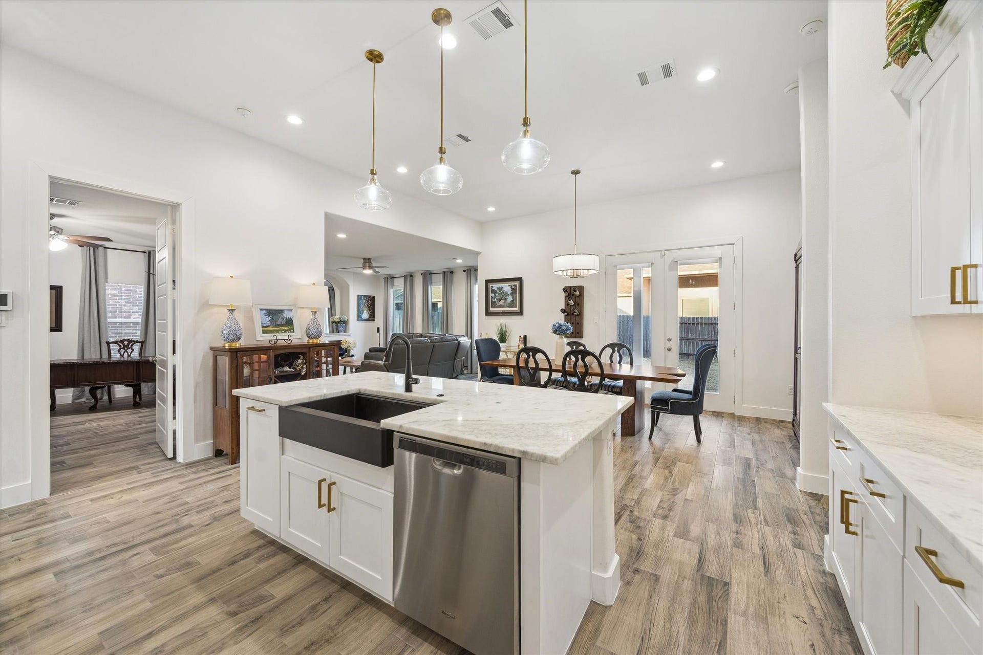 This angle showcases the kitchen island in harmony with the dining area and living room. The unique dark farmhouse sink provides a striking contrast to the kitchens overall light color palette, adding both style and character. A truly inviting and functional space youll love.