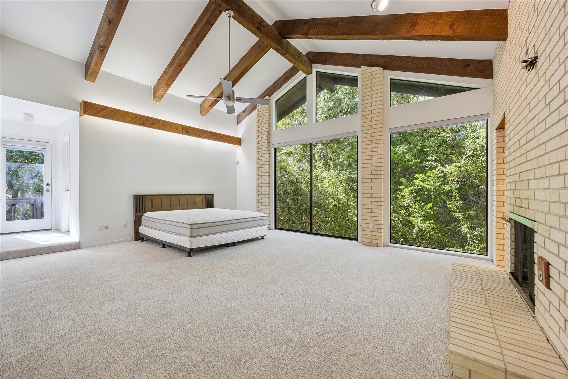104 Gershwin Drive, Houston, TX 77079 Spacious primary bedroom features a soaring vaulted ceiling w/ exposed wood beams, brick fireplace & walls of windows that fill the room w/natural light. The door to the left leads out to a large porch for you to enjoy.