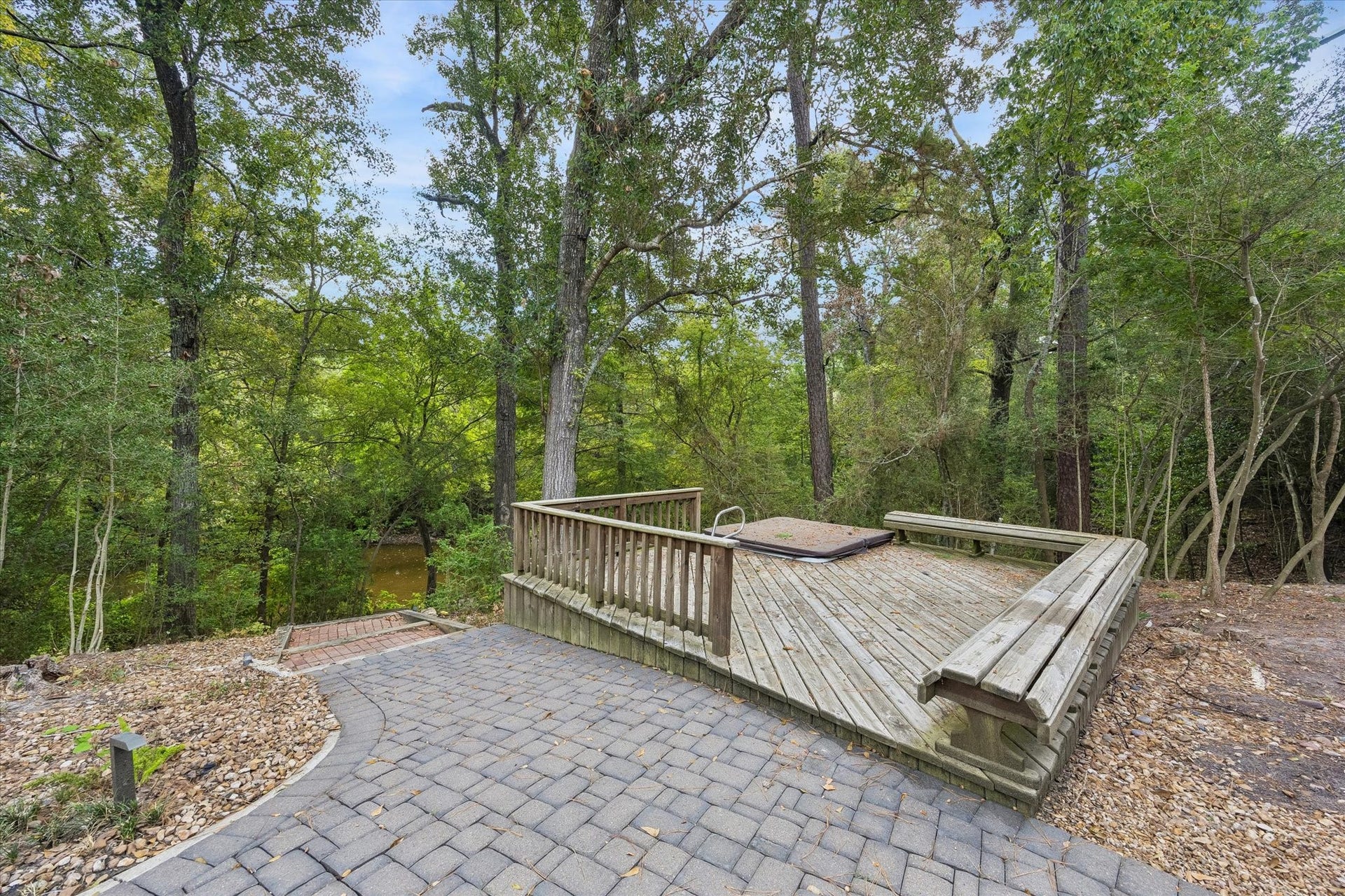 104 Gershwin Drive, Houston, TX 77079 Wooded outdoor retreat featuring a spacious deck w/built-in seating & hot tub/spa, surrounded by mature trees & overlooking the lake beyond.