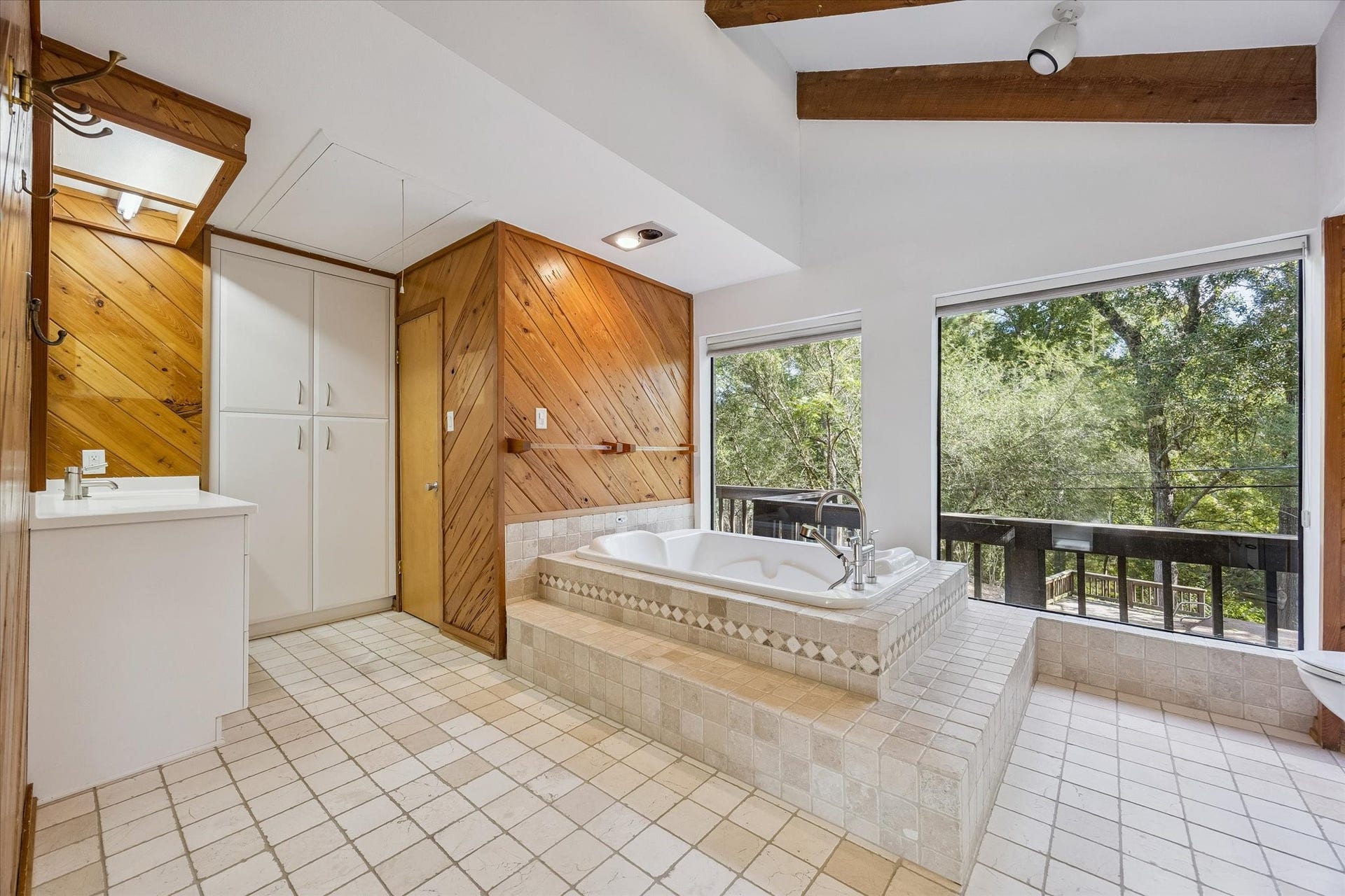 104 Gershwin Drive, Houston, TX 77079 Primary bath features a jetted soaking tub framed by large windows, vaulted beamed ceiling & warm wood accents, plus convenient access to a walk-in closets and built-in shelving.
