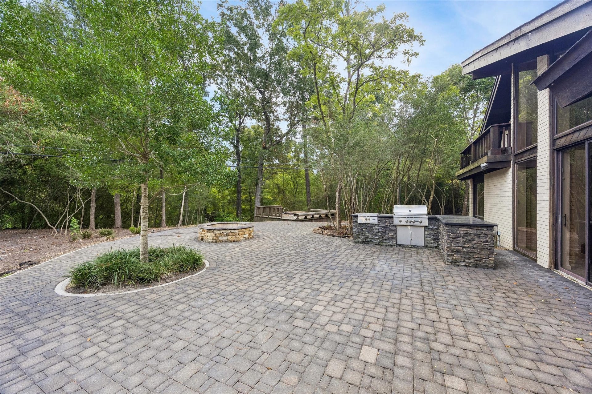 104 Gershwin Drive, Houston, TX 77079 Expansive outdoor entertaining area features a large paver patio, built-in outdoor kitchen & fire pit, all surrounded by the propertys beautiful wooded setting.