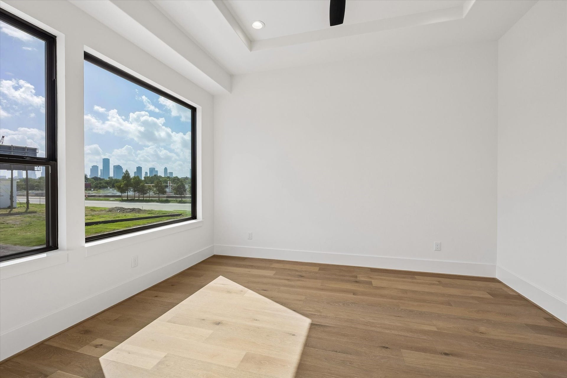 335 Harvard Street, Houston, TX 77007 Downtown skyline views become a standout feature of this secondary bedroom, framed by oversized black windows. A tray ceiling and hardwood floors carry the homes clean, contemporary design upstairs.