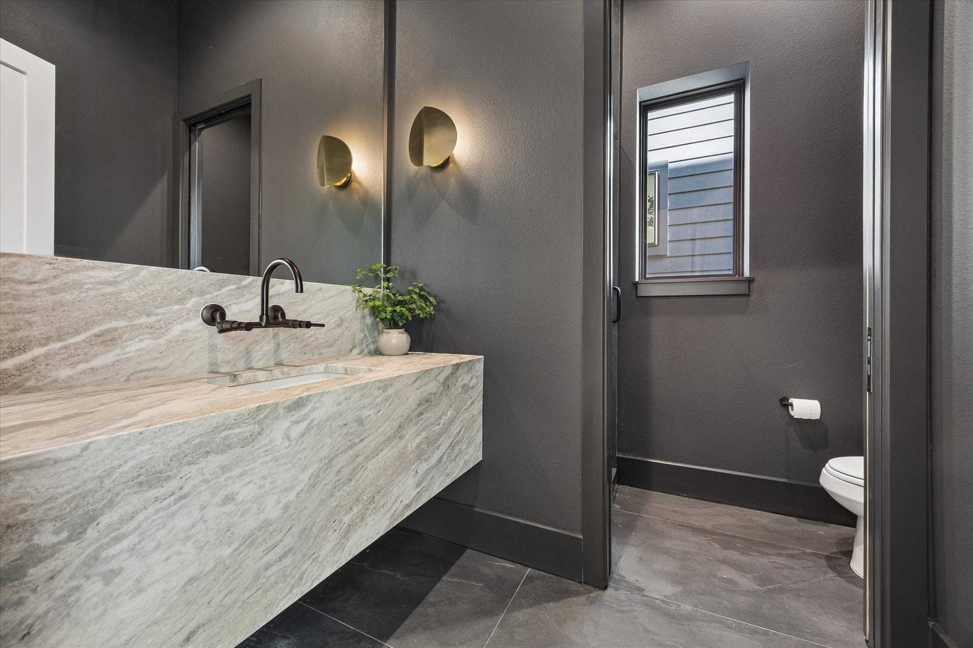 335 Harvard Street, Houston, TX 77007 Moody and memorable, the powder bath pairs deep charcoal walls with a dramatic stone vanity, integrated sink and wall mounted faucet. Sculptural brass sconces bring warmth to the richly layered palette.