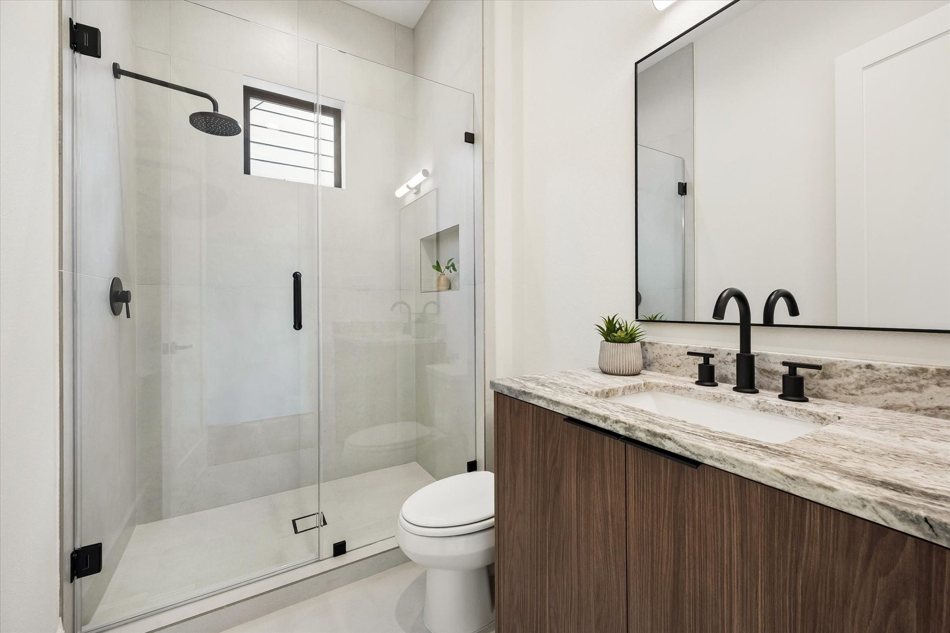 335 Harvard Street, Houston, TX 77007 Serving both a secondary bedroom and the loft, this hall bath features a glass enclosed walk in shower, warm wood vanity, stone countertop and matte black fixtures for a crisp, modern finish.
