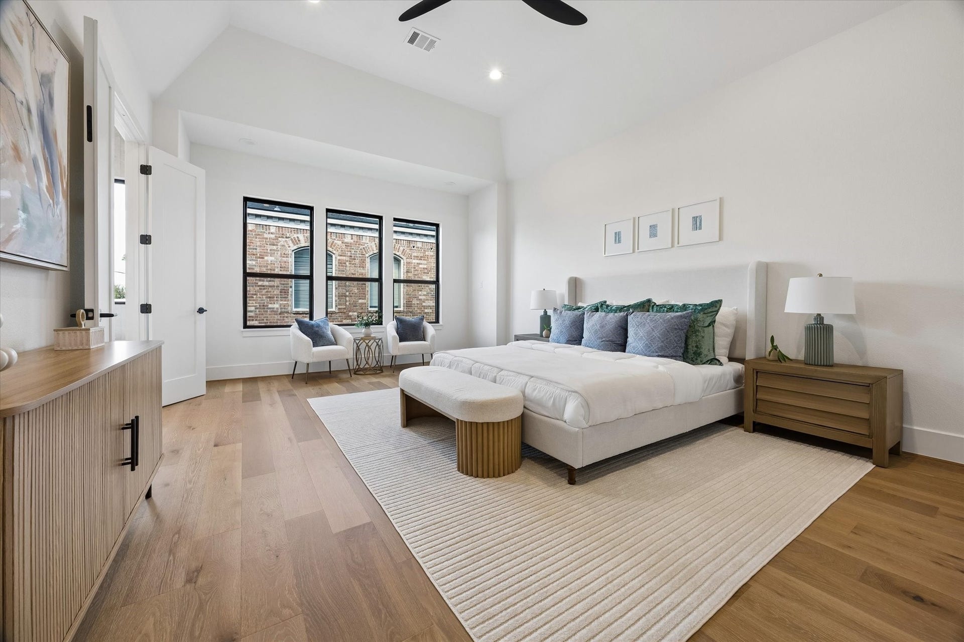 335 Harvard Street, Houston, TX 77007 Vaulted ceilings give the primary suite an airy sense of scale, while a trio of black framed windows brings in natural light. Hardwood floors continue into the retreat for a cohesive finish.