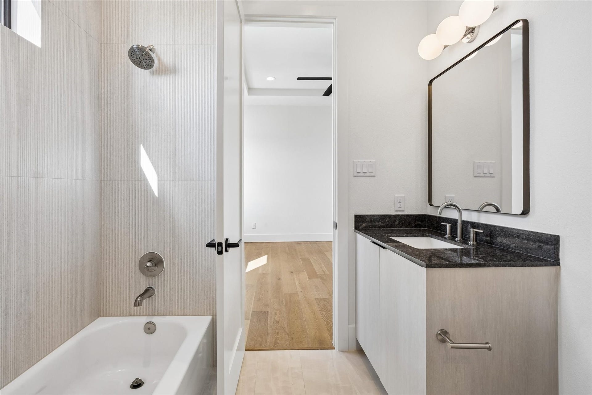 335 Harvard Street, Houston, TX 77007 Contemporary finishes continue into the secondary ensuite, pairing a dark stone countertop with light wood cabinetry and softly textured tile surrounding the tub and shower.