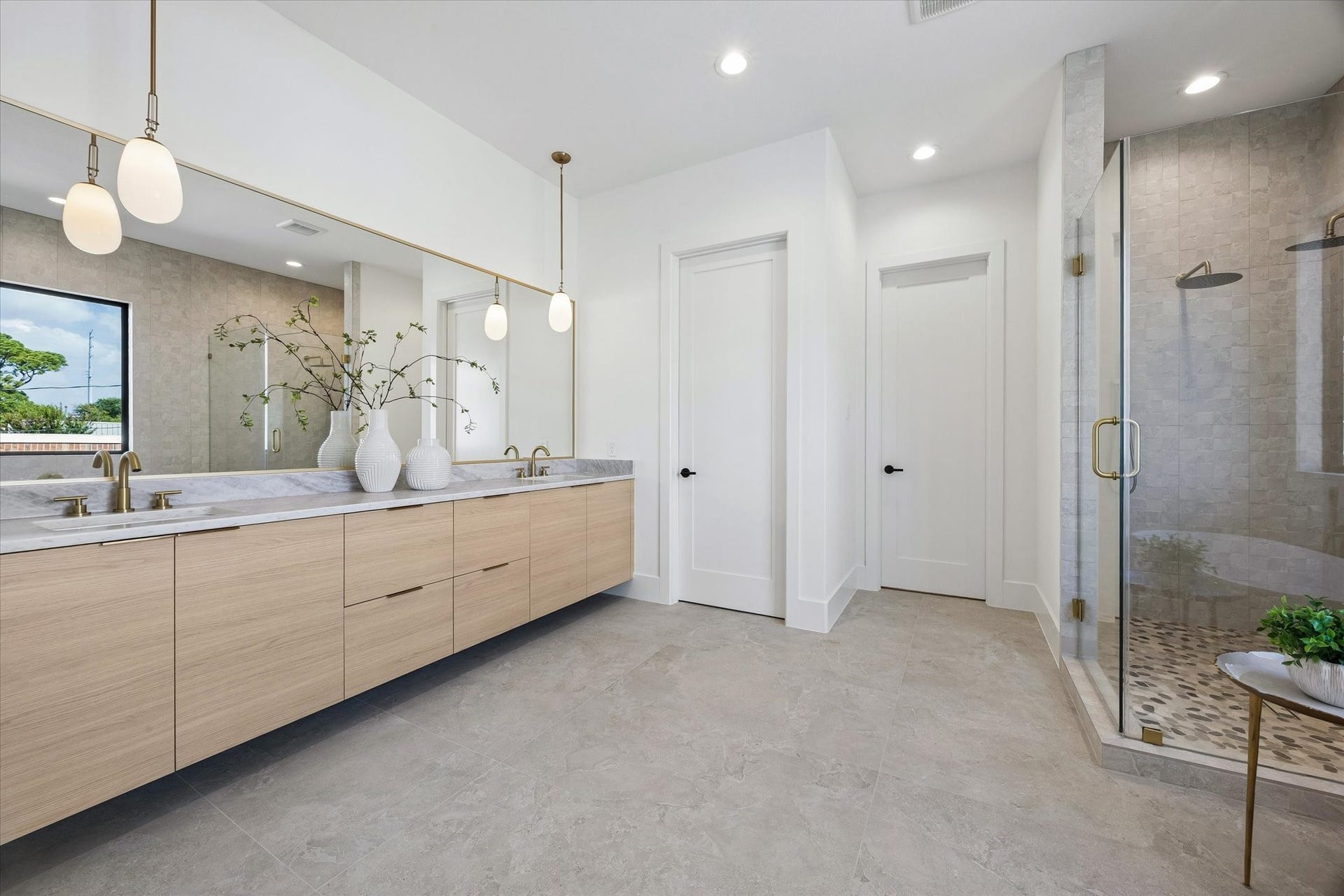 335 Harvard Street, Houston, TX 77007 An expansive floating vanity stretches beneath an oversized mirror, pairing warm wood cabinetry with stone counters and understated brass fixtures. The glass enclosed shower continues the neutral stone palette for a cohesive, spa inspired finish.