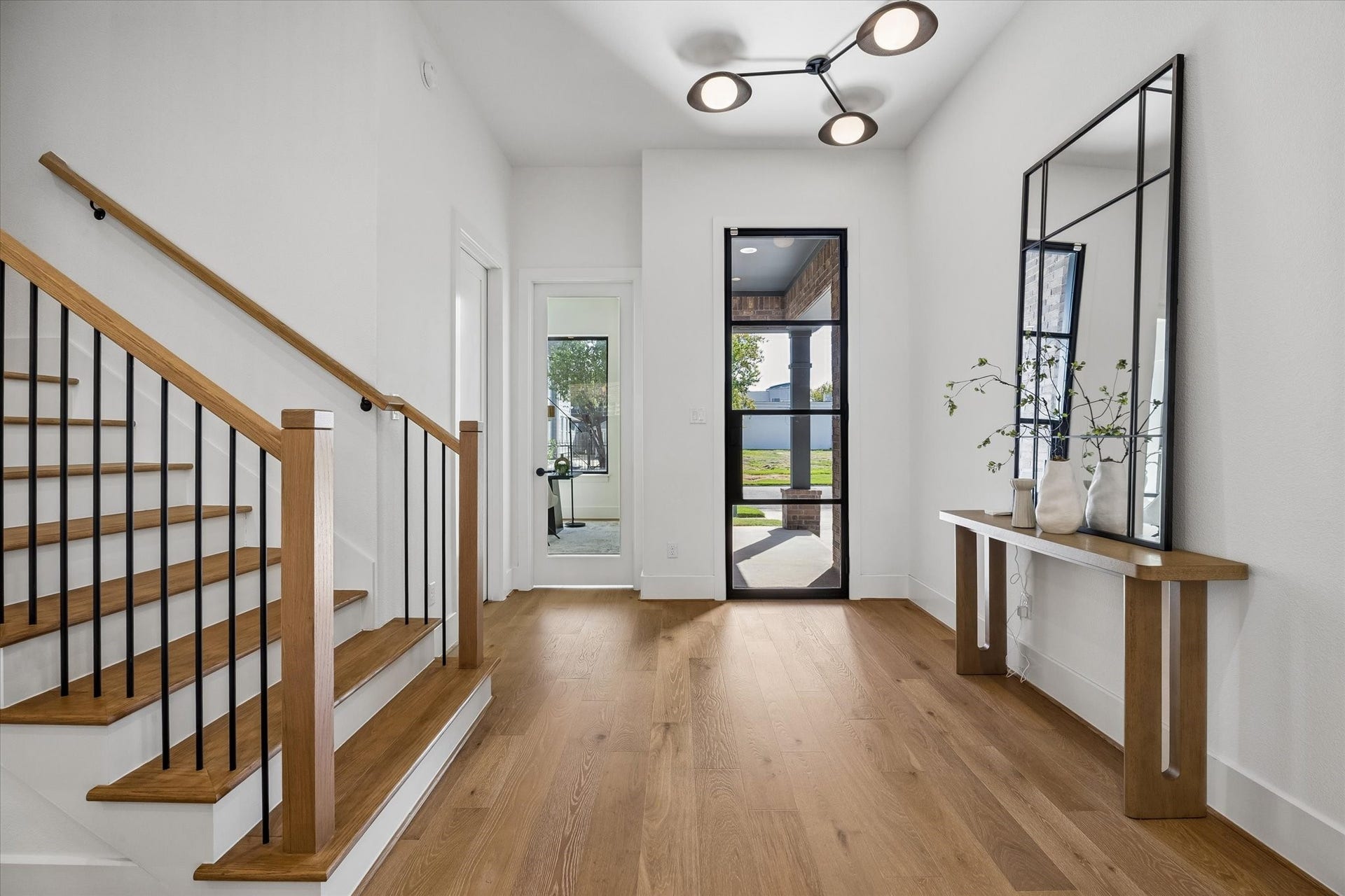 335 Harvard Street, Houston, TX 77007 Warm wood flooring and a streamlined staircase with black metal balusters bring contrast and character to the light filled entry. A modern statement fixture and tall glass front door introduce the homes clean, contemporary design from the start.