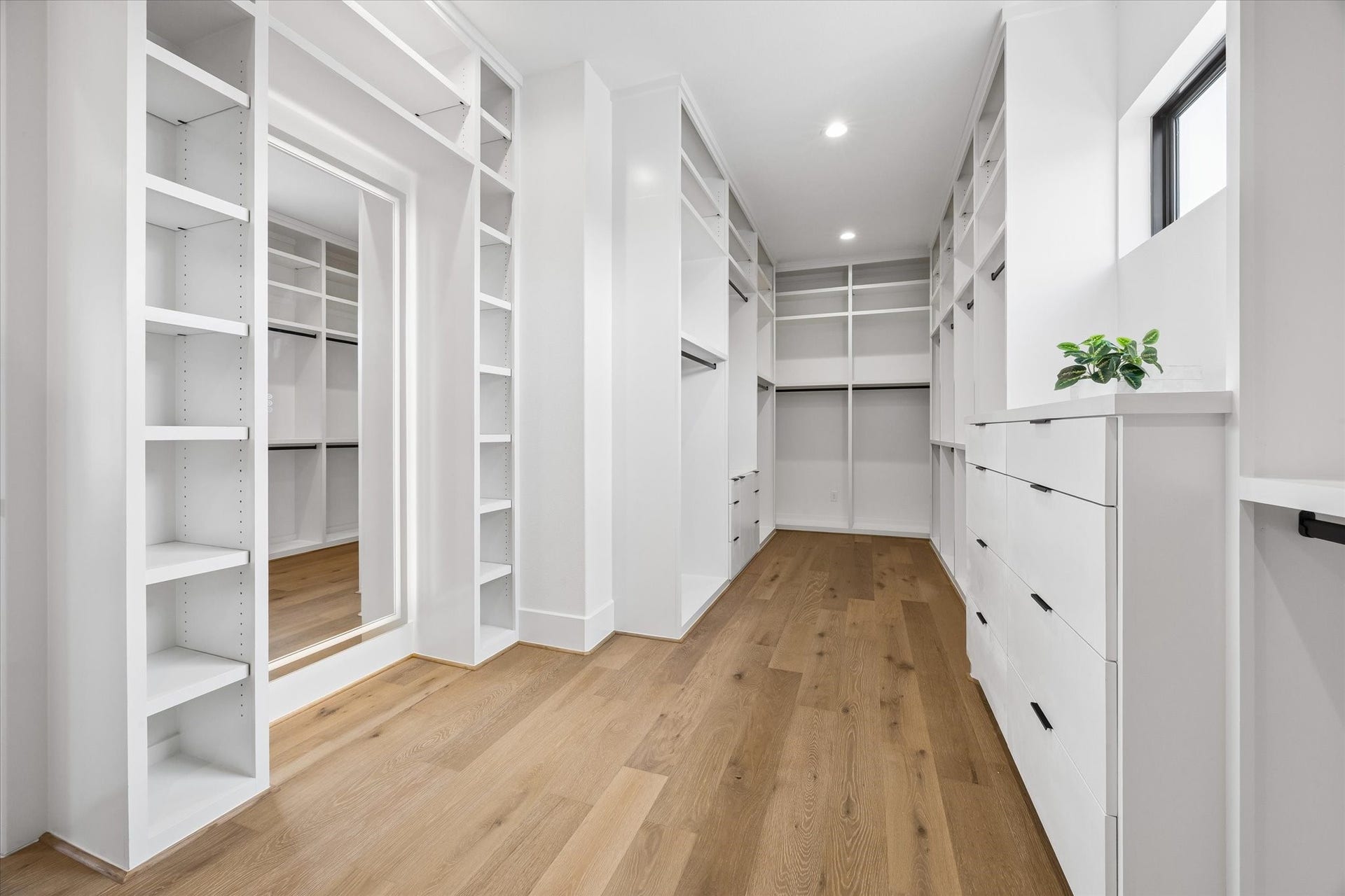 335 Harvard Street, Houston, TX 77007 Custom built ins transform the primary walk in closet with extensive shelving, hanging space, integrated drawers, and a full length mirror. A window introduces natural light while hardwood flooring carries through from the primary suite.