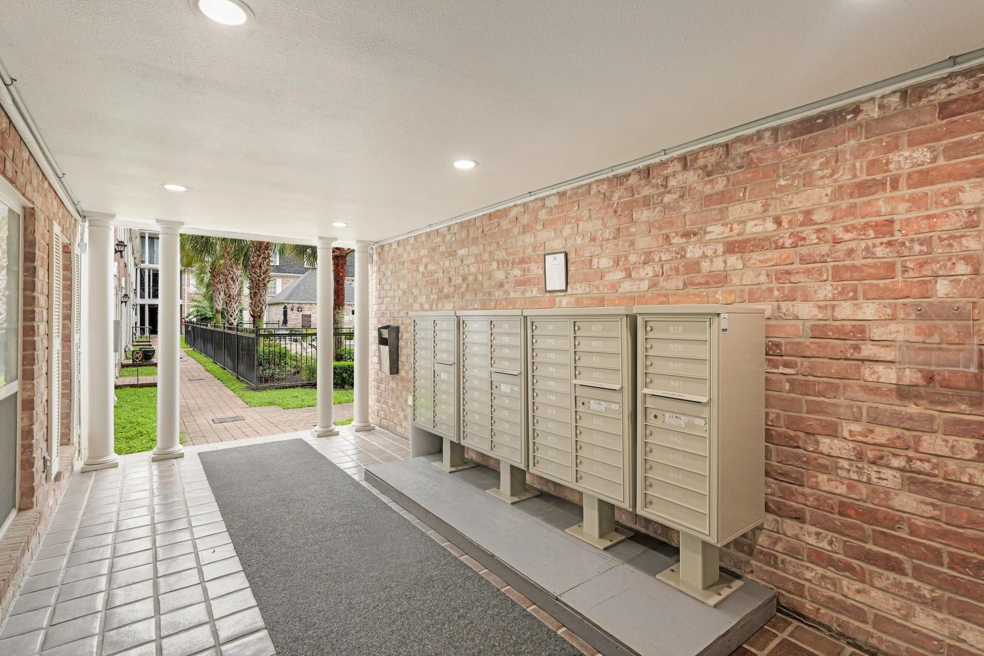 355 N Post Oak Lane, #839, Houston, TX 77024 Charming covered walkway with secure mailbox area and classic brick walls, leading to a beautifully landscaped courtyard.