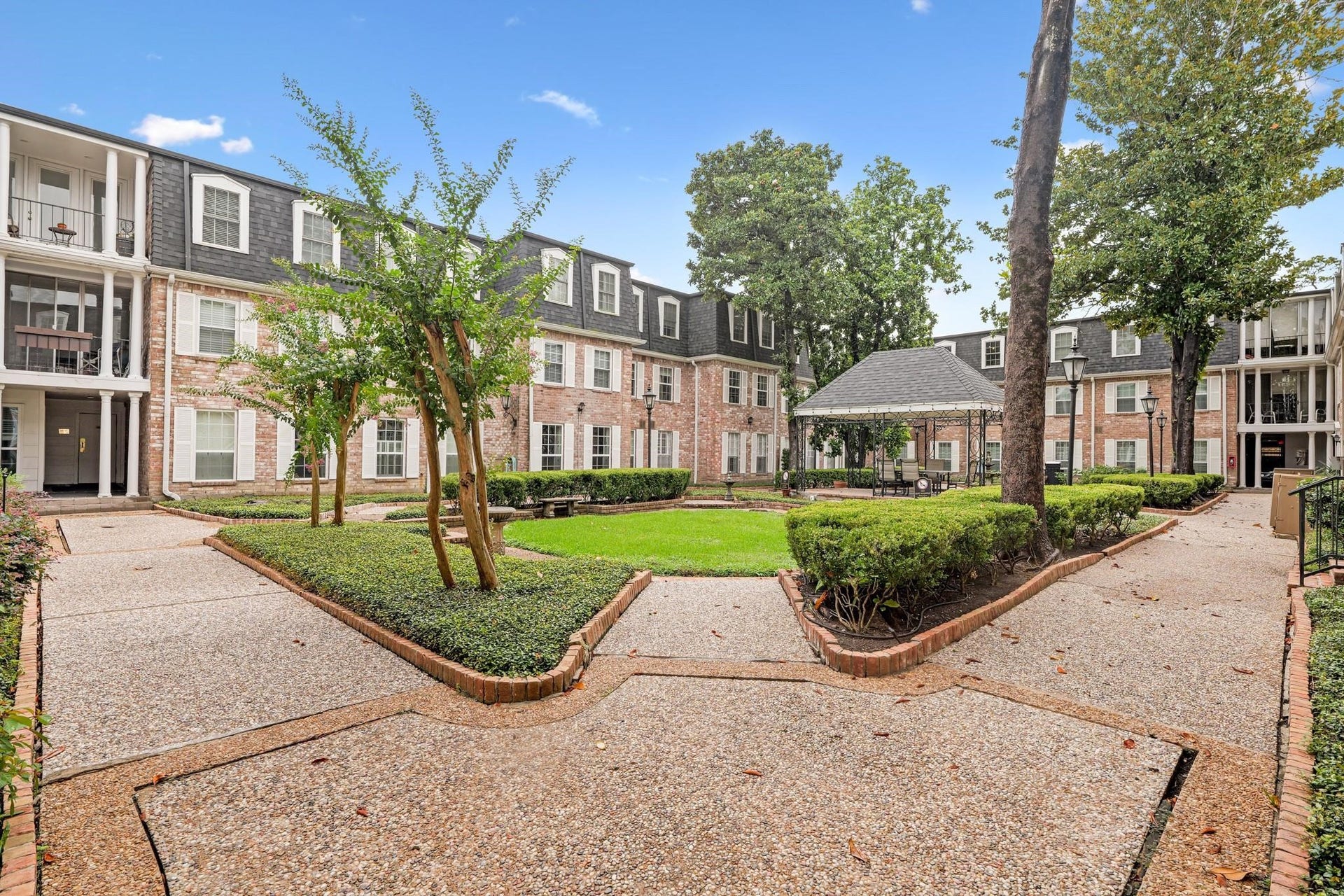 355 N Post Oak Lane, #839, Houston, TX 77024 Charming courtyard view of a classic brick apartment complex featuring a lush central lawn, mature trees, and a cozy gazebo, offering a serene and inviting atmosphere.