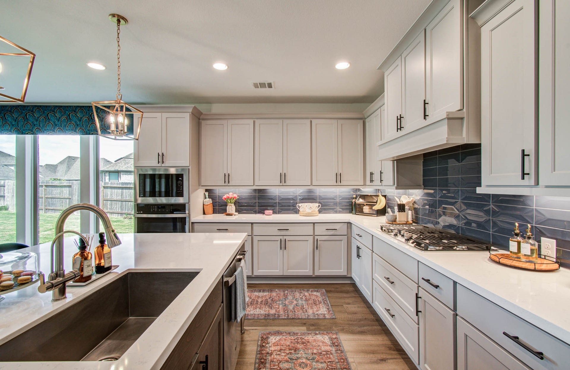 24430 Switchgrass Valley Way, Katy, TX 77493 A modern kitchen with sleek white cabinetry, a spacious island featuring a sink, and stainless steel appliances is beautifully illuminated by large windows and stylish lighting, creating an inviting and functional space perfect for cooking and entertaining.