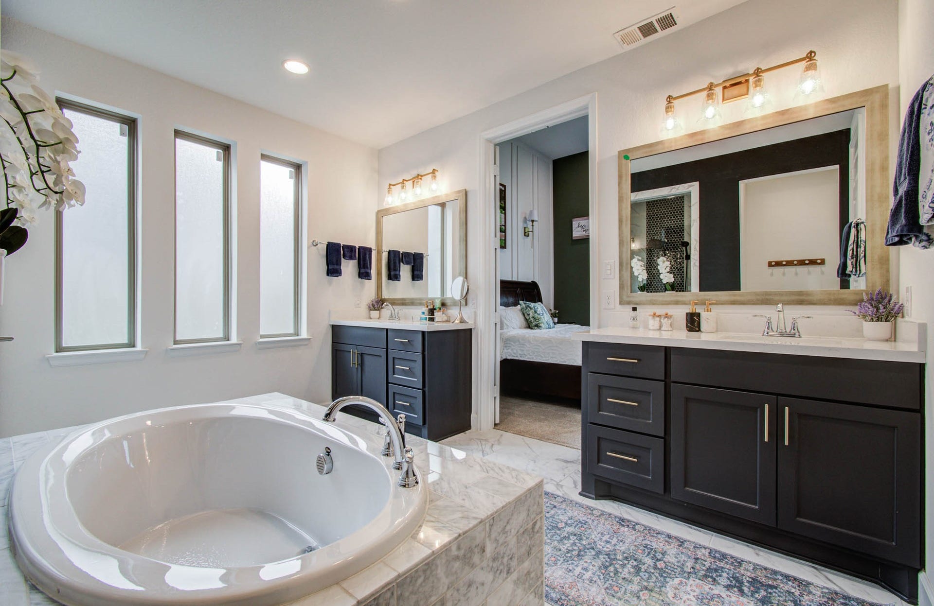 24430 Switchgrass Valley Way, Katy, TX 77493 This elegant bathroom features a spacious bathtub, dual vanities with dark cabinetry, and large windows for natural light. It offers a modern design with stylish fixtures, leading into a connected bedroom for convenience.