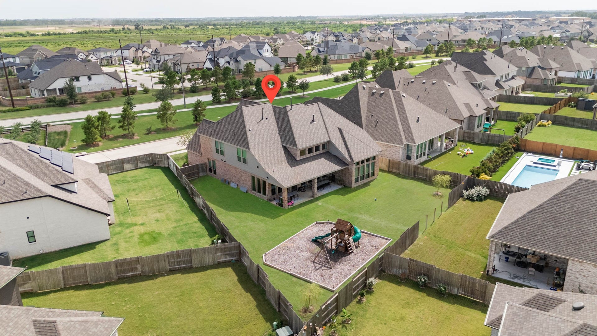 24430 Switchgrass Valley Way, Katy, TX 77493 This aerial photo showcases a spacious, fenced backyard with a playset, offering a large lawn area. The home features a modern roof design, and the neighborhood is filled with similar, well-maintained houses, indicating a vibrant community.