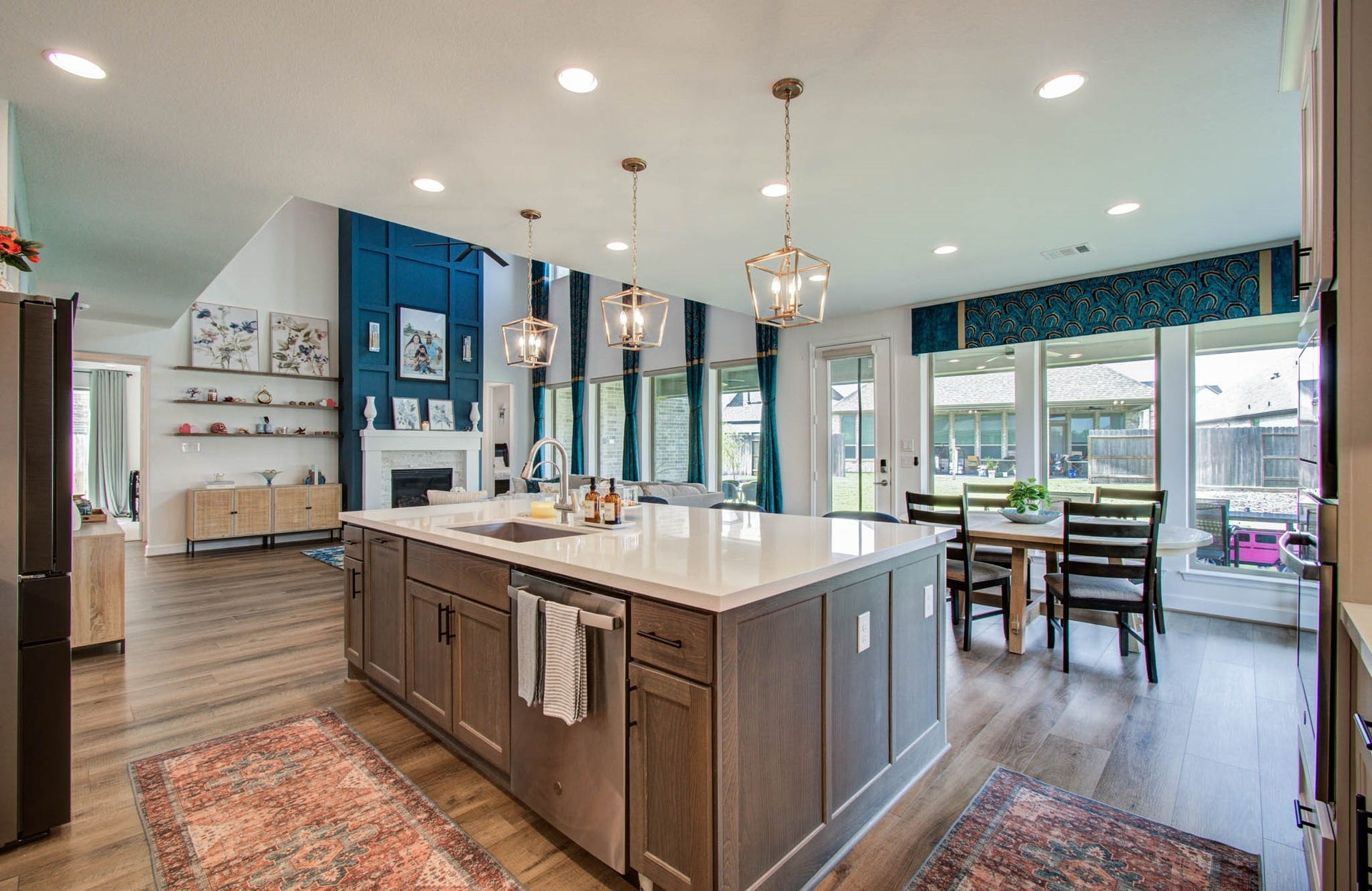 24430 Switchgrass Valley Way, Katy, TX 77493 Experience the grandeur of a high-ceilinged living area accentuated by a bold blue wall with a cozy fireplace, bathed in natural light from large windows offering serene views of the fenced backyard.