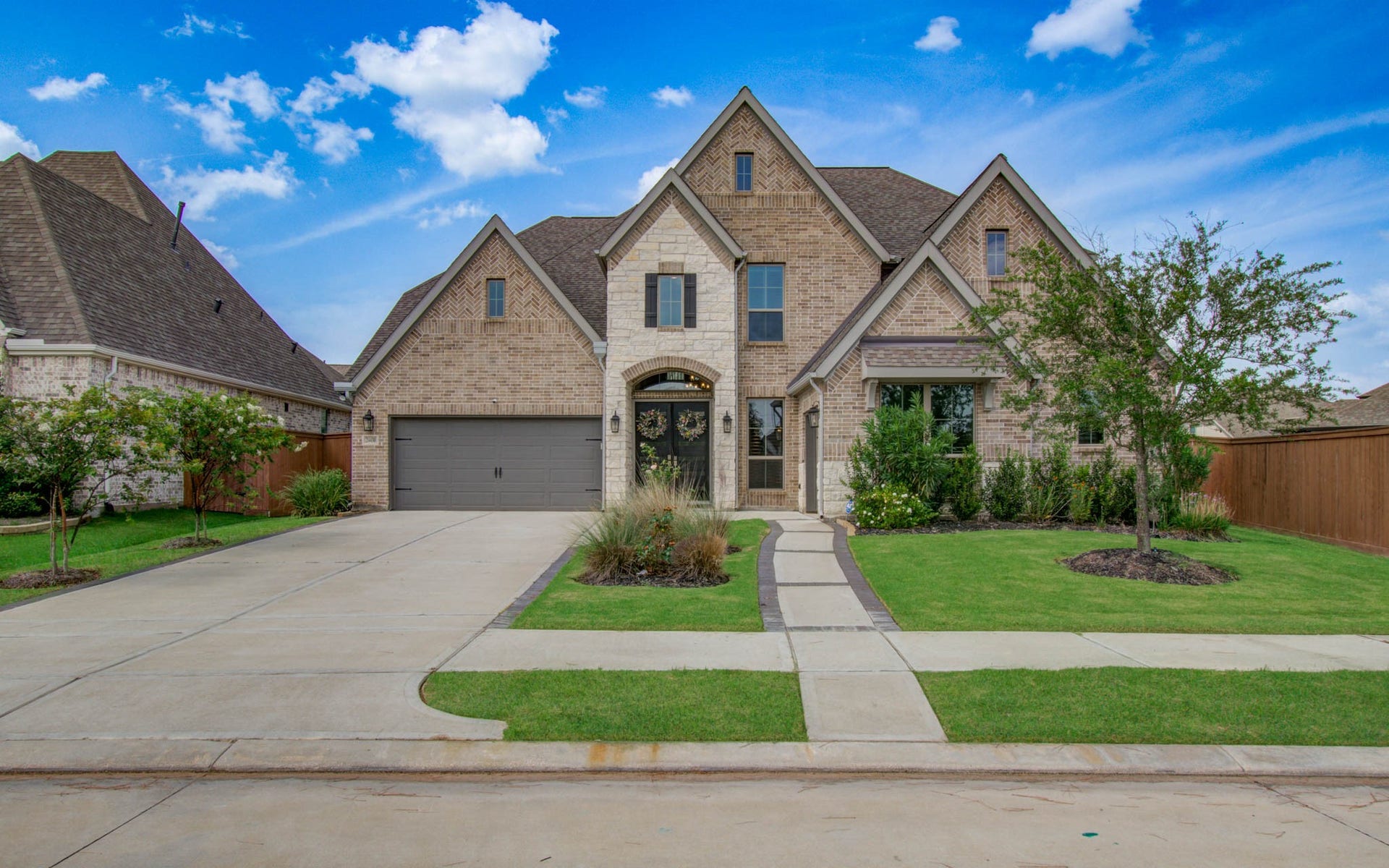 24430 Switchgrass Valley Way, Katy, TX 77493 This is a beautiful two-story brick home with a steeply pitched roof, featuring a spacious driveway leading to a two-car garage. The well-maintained front yard includes a paved walkway, manicured lawn, and mature trees, offering excellent curb appeal.