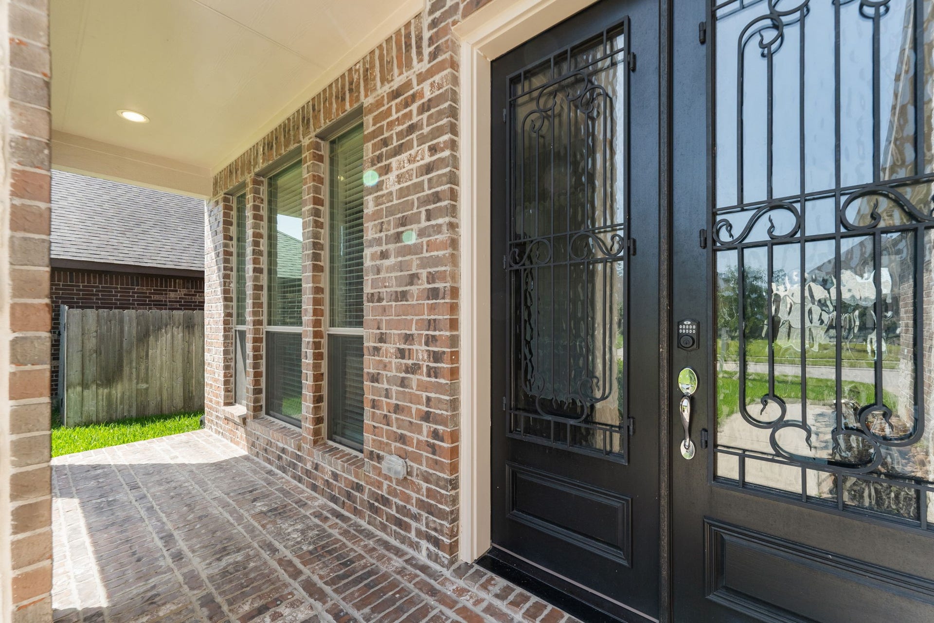This photo showcases a welcoming entryway with a brick exterior, large windows, and a decorative black front door, offering a blend of elegance and security.