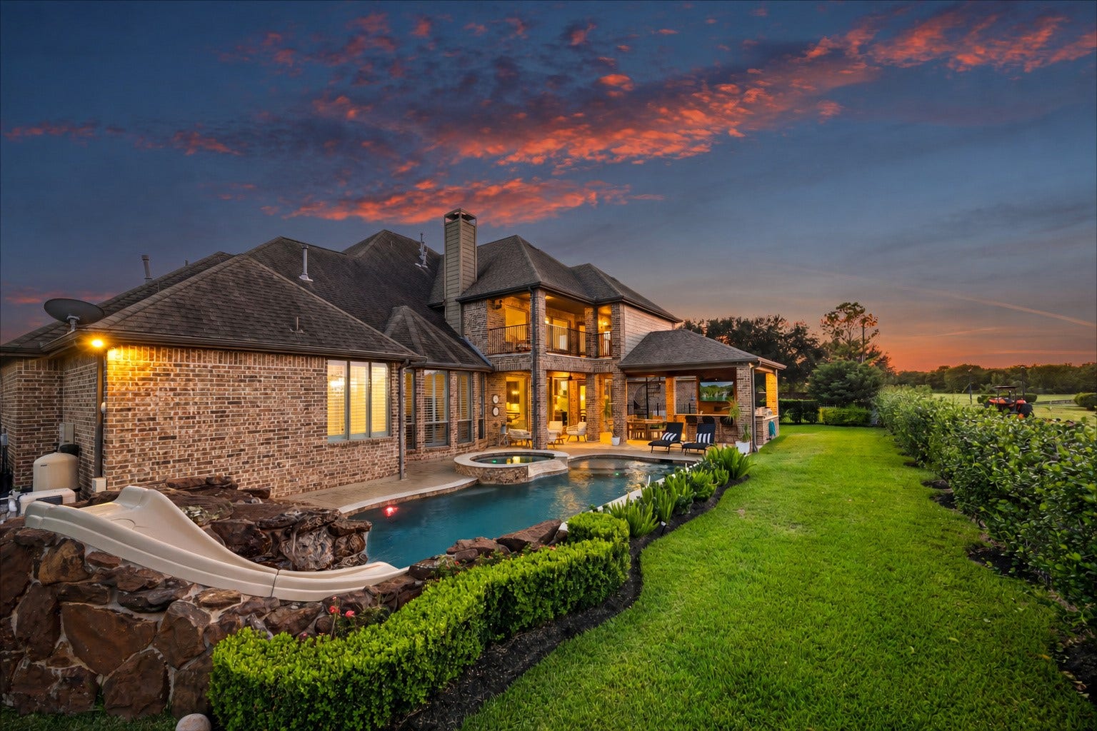 8642 Chickasaw Plum Way, Katy, TX 77494 Resort-style backyard at dusk featuring a sparkling pool, outdoor kitchen, and expansive green space. Heated PebbleTec chlorine pool and outdoor kitchen with Alfresco grill and Alfresco flat grill.