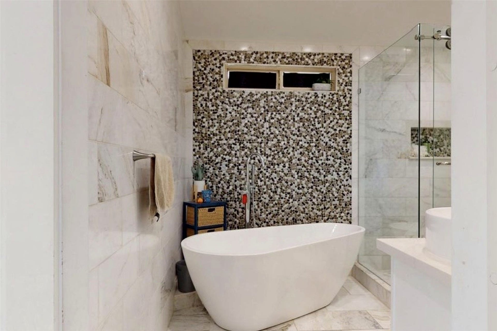 827 Dondell Street, Channelview, TX 77530 827 Dondell, Spa inspired primary bedroom, freestanding soaking tub with modern floor-mounted faucet, pebble mosaic accent wall and mable tile through out the walls and flooring. A glass enclosed walk-in shower with a built-in niche.