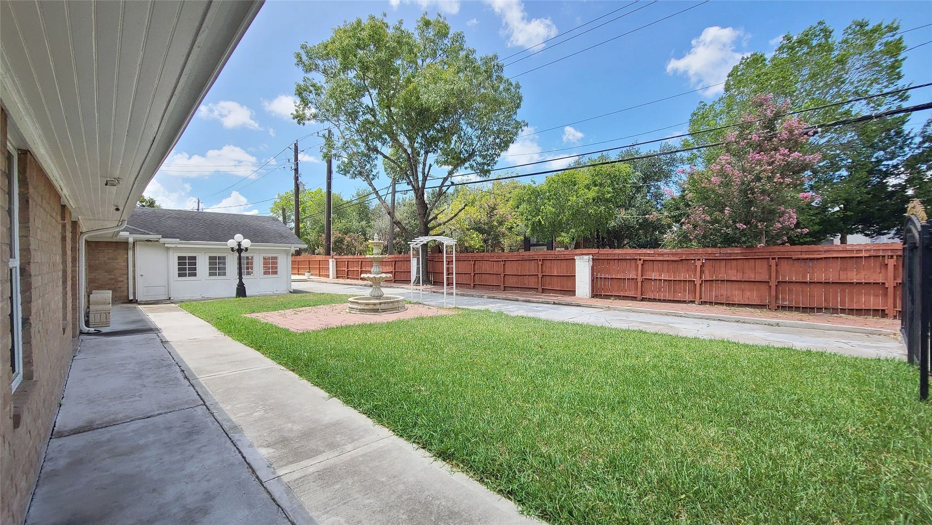 902 Ashford Parkway, Houston, TX 77077 Charming single-story home with a classic brick exterior, featuring a welcoming courtyard with a central fountain and elegant lamppost, surrounded by lush greenery.