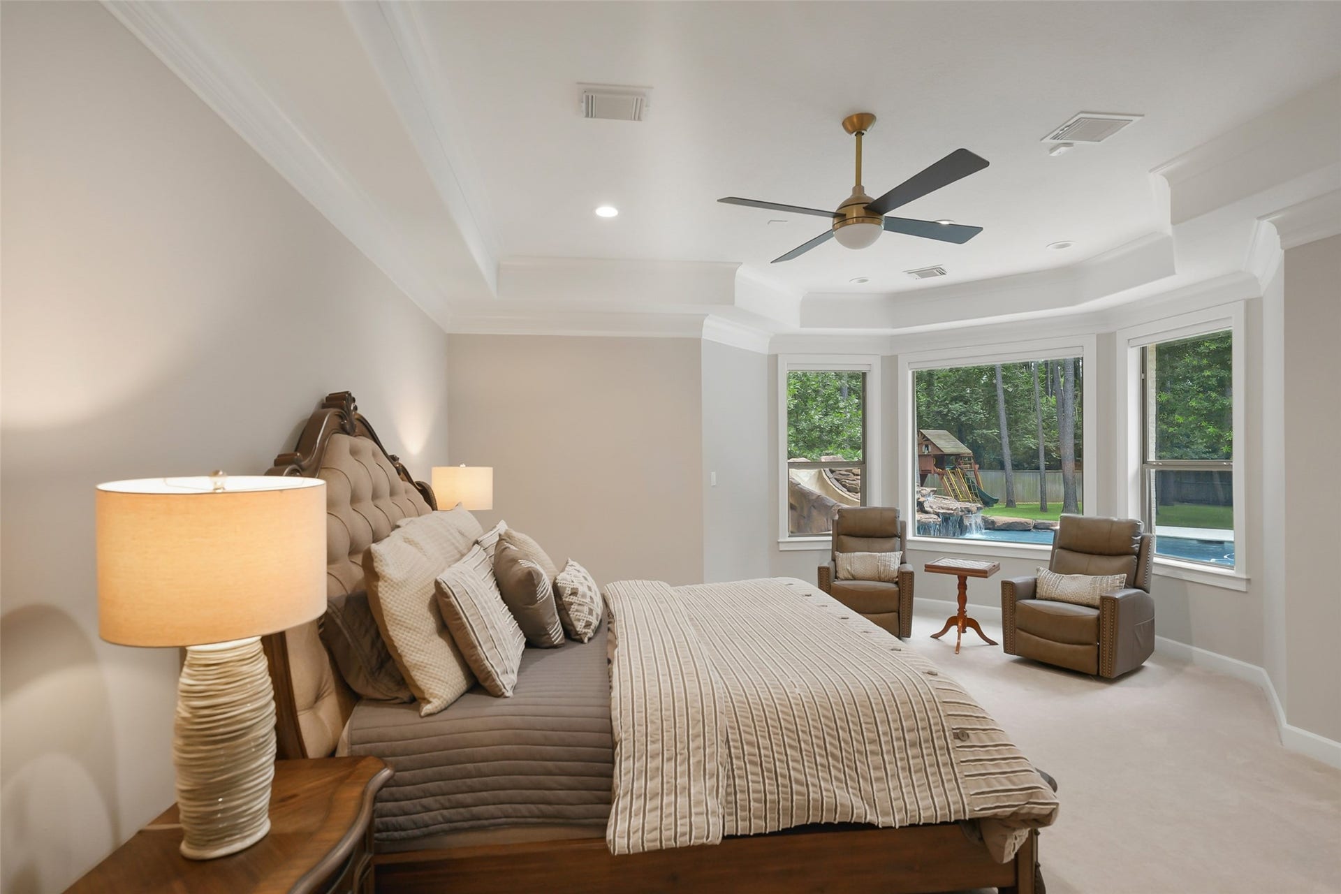 19 Harmony Links Place, The Woodlands, TX 77382 The primary bedroom is truly a retreat from everyday life. A seating area surrounded by windows with a view of the lush backyard is the perfect place to wind down before sleep.