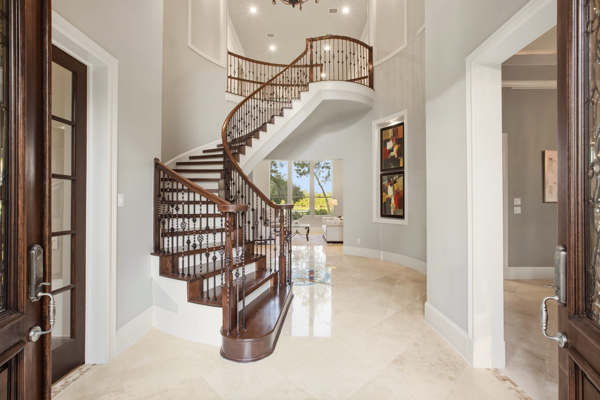 3518 River Forest Drive, Richmond, TX 77406 Elegant entryway featuring a grand spiral staircase with rich wood accents and ornate railings, complemented by polished marble floors and modern art, leading to a bright living area.
