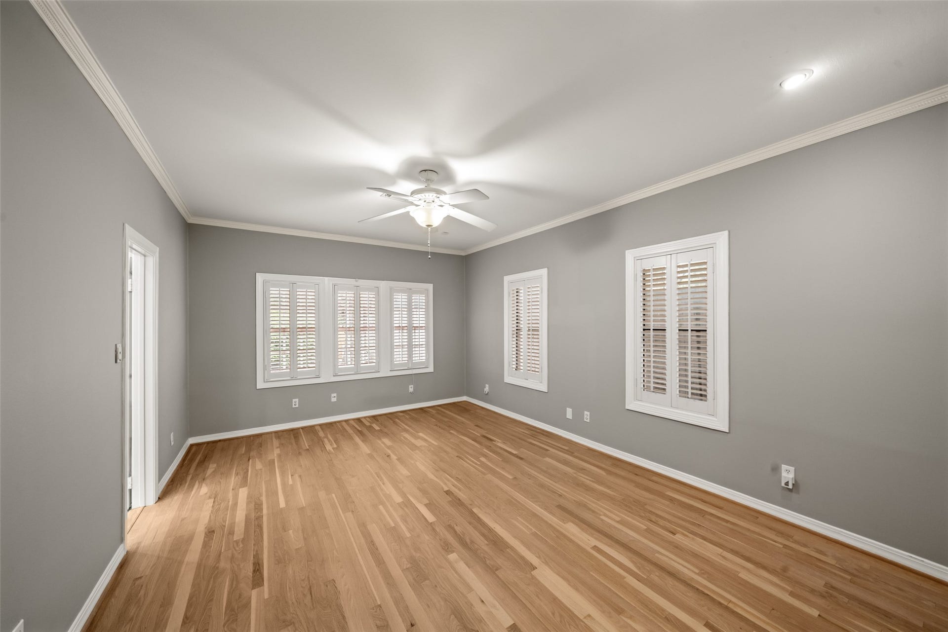 Spacious primary bedroom featuring wood floors, crown molding, and windows with shutters.