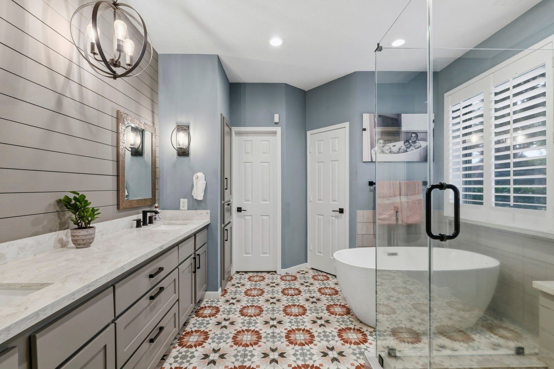 Renovated bathroom featuring a spacious double vanity with quartz countertops, a luxurious freestanding soaking tub, shiplap accent walls, beautiful flooring, and modern designer touches in the spa-inspired retreat.