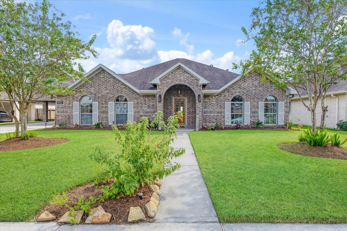 Welcome to 6602 Texoma Drive in Lakeland, Manvel, TX 77578. This lakefront home features a brick exterior, covered entry, arched windows, mature trees and a landscaped front lawn.