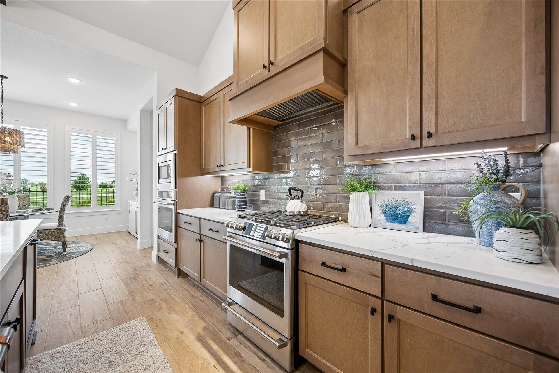 Beautifully appointed, the kitchen showcases a custom wood vent hood, an earthy-toned designer subway tile backsplash, and elegant under-cabinet lighting. Upgraded GE Caf stainless steel appliances complement the space, while overlooking the backyard's scenic views.