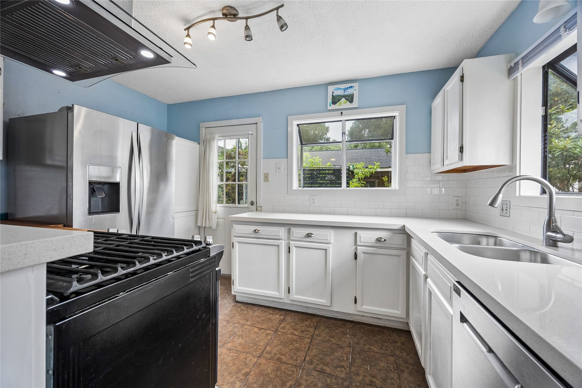 1039 Dunbar Street, Houston, TX 77009 A bright, functional kitchen offers white cabinetry and countertops, stainless-steel refrigerator and dishwasher, a gas range, and windows overlooking the greenery outside