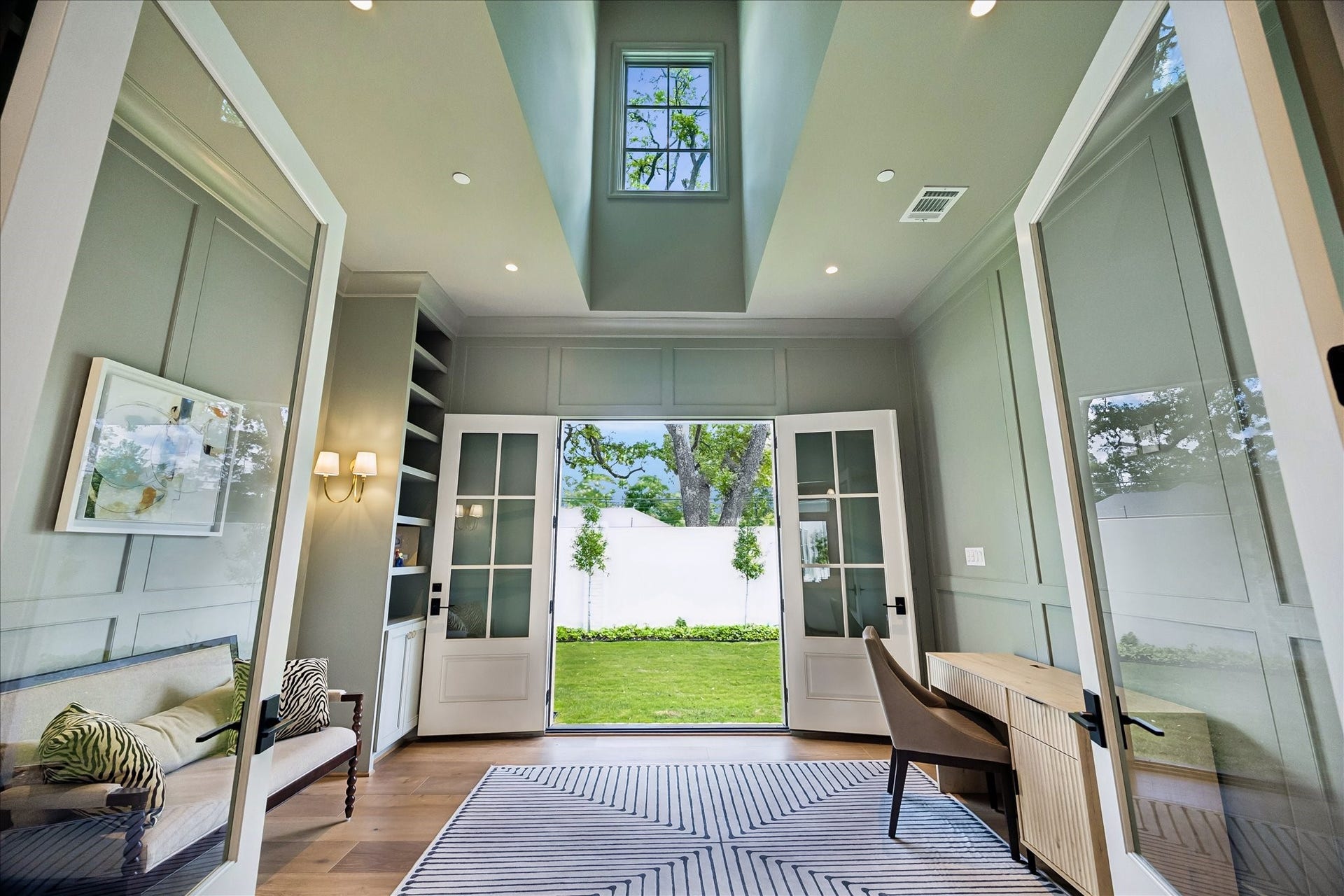 10801 Long Shadow Lane, Hunters Creek Village, TX 77024 Framed by glass divided light double doors, this impressive study features soaring ceiling with a dramatic ceiling detail and overhead window, allowing natural light to pour in from above. Paneled walls, custom built-ins, and elegant sconces add architectural interest, while French doors open directly to the side yard, creating a seamless indoor-outdoor connection.