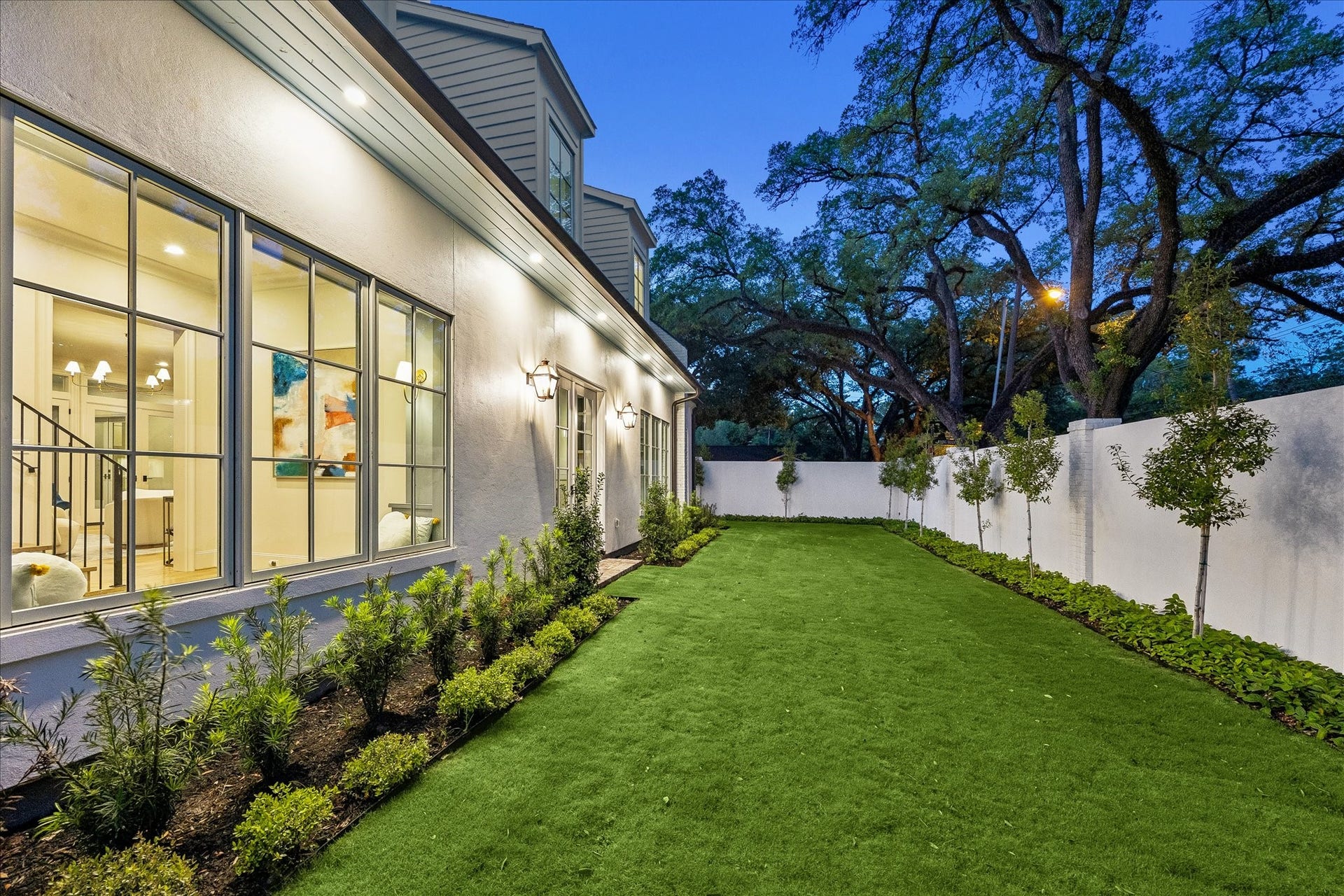 10801 Long Shadow Lane, Hunters Creek Village, TX 77024 Another view of the landscaped grounds featuring lush turf, manicured landscaped beds & privacy wall. Large windows line the home, creating a seamless connection to the outdoor spaces while landscape lighting & trees enhance the setting.