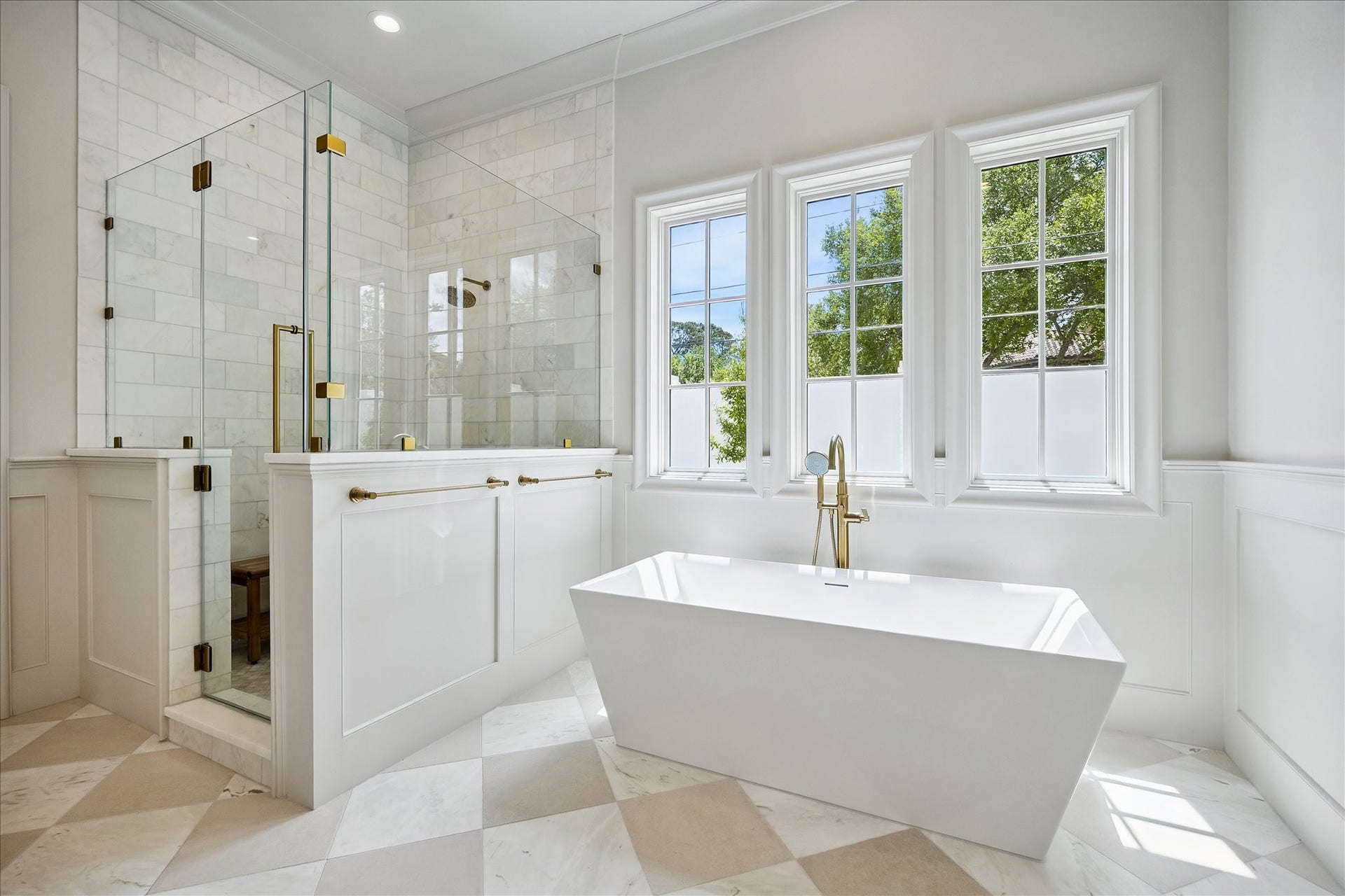 10801 Long Shadow Lane, Hunters Creek Village, TX 77024 The spa-inspired primary bath showcases timeless finishes, featuring marble tile surround and elegant fixtures. A freestanding soaking tub is perfectly positioned beneath a wall of windows, while the oversized walk-in shower offers frameless glass enclosure and gorgeous tilework to the ceiling.