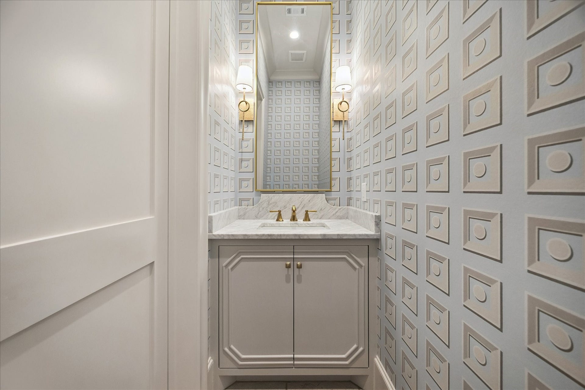 10801 Long Shadow Lane, Hunters Creek Village, TX 77024 Elegant powder bath featuring a marble countertop and backsplash, complemented by a gorgeous custom vanity with polished hardware. Designer wallcoverings add striking dimension, while a framed mirror and beautiful sconces create a sophisticated, elevated ambiance.