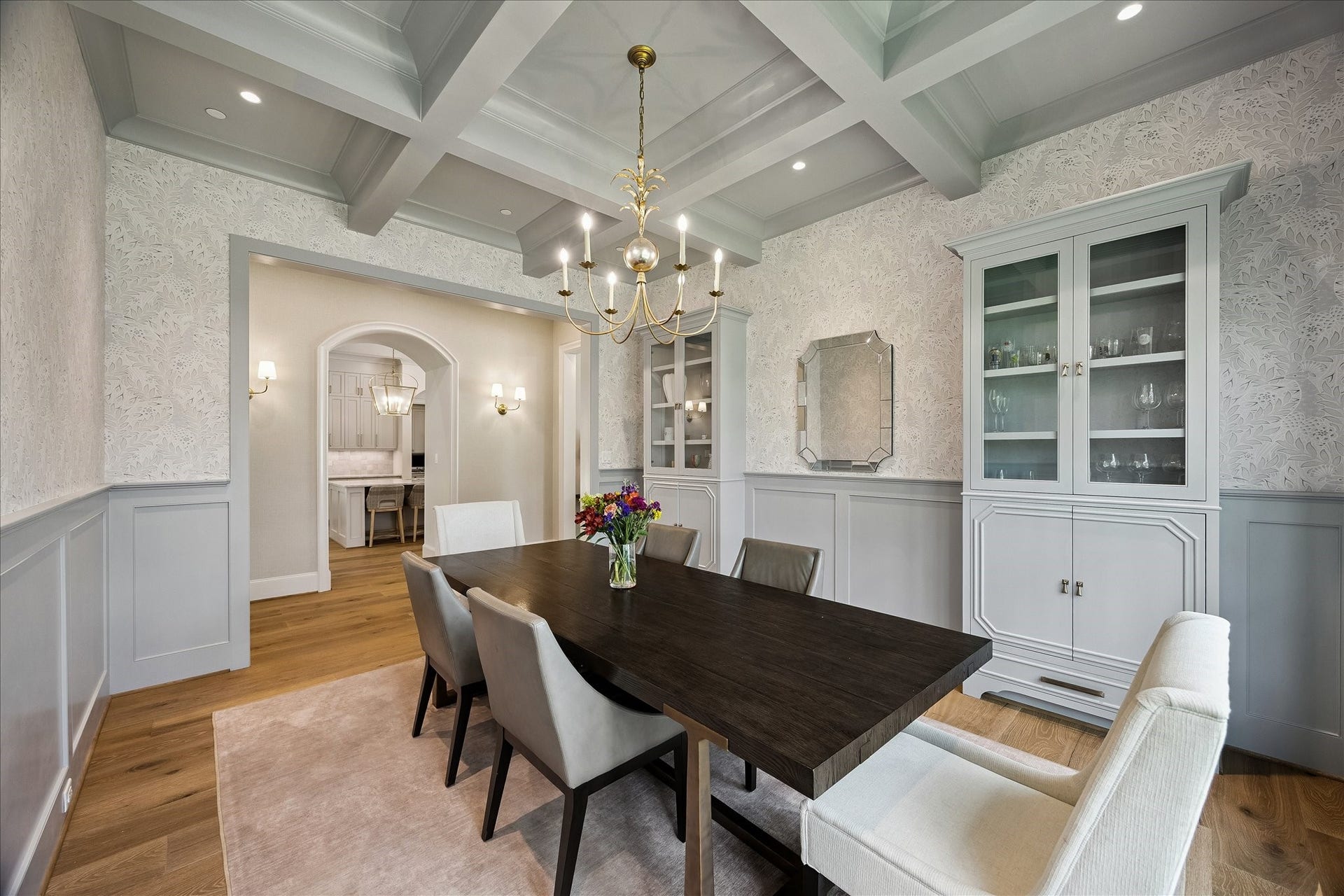 10801 Long Shadow Lane, Hunters Creek Village, TX 77024 View of dining room toward the kitchen entry showcasing the architectural archway framed with sconce lighting and seamless flow to the kitchen. Designer lighting and tailored millwork enhance the dining rooms elevated design.