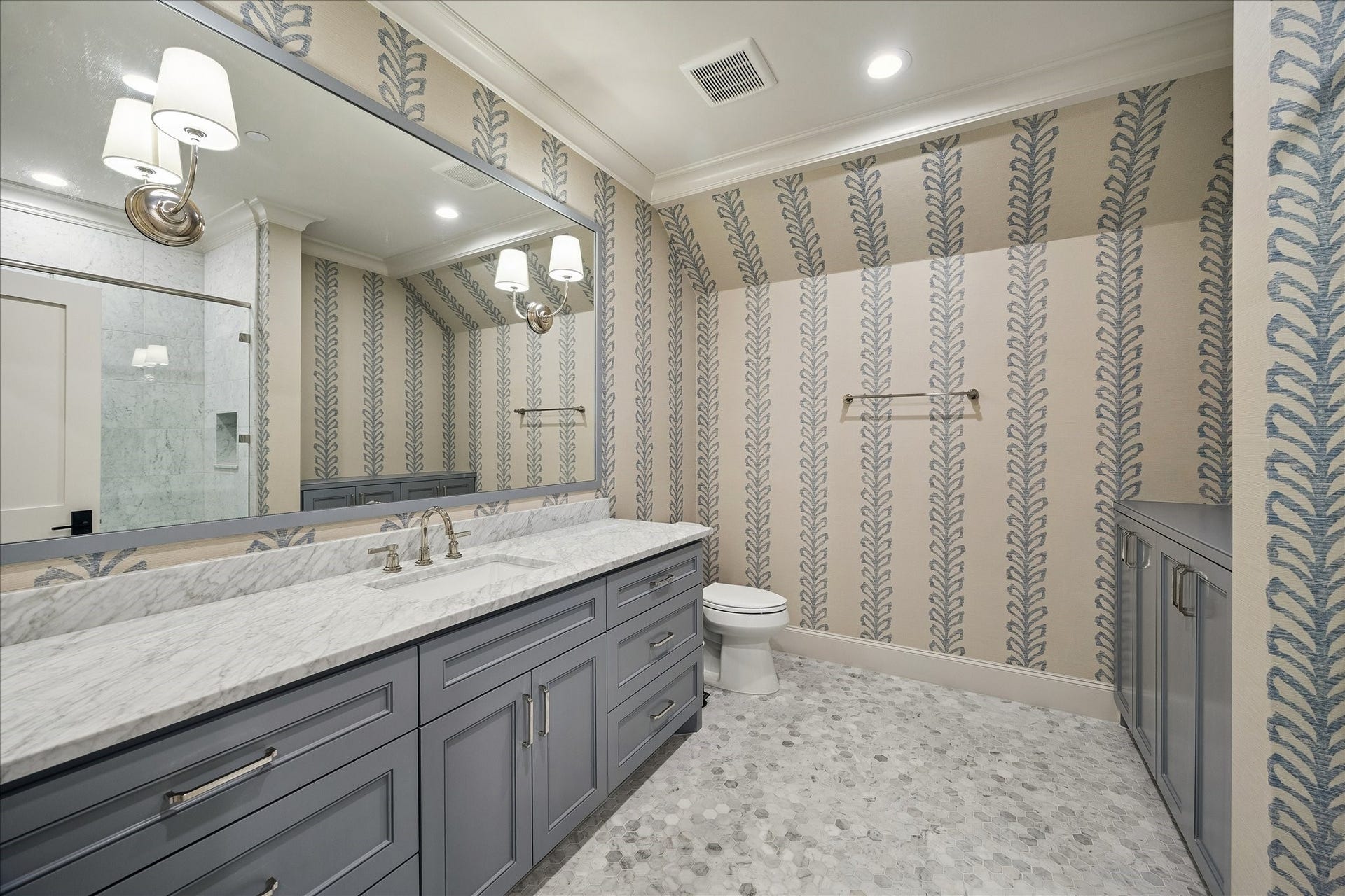 10801 Long Shadow Lane, Hunters Creek Village, TX 77024 Beautifully designed secondary bath up featuring a marble slab countertop, custom painted cabinetry, and a sleek undermount sink paired with polished fixtures. Designer wallpaper adds a beautiful look, while the mosaic tile flooring brings subtle texture and visual interest. Thoughtfully finished with crown molding and quality detailing throughout, creating a stylish and functional space.