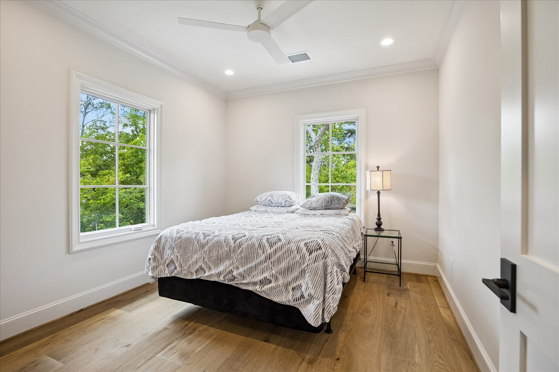 10801 Long Shadow Lane, Hunters Creek Village, TX 77024 Bedroom of the light-filled mother-in-law/guest suite featuring French white oak wide plank flooring, crown molding, recessed lighting and ceiling fan, along with large windows that bring in abundant natural light and treetop views. A clean, airy palette creates a welcoming and comfortable retreat.