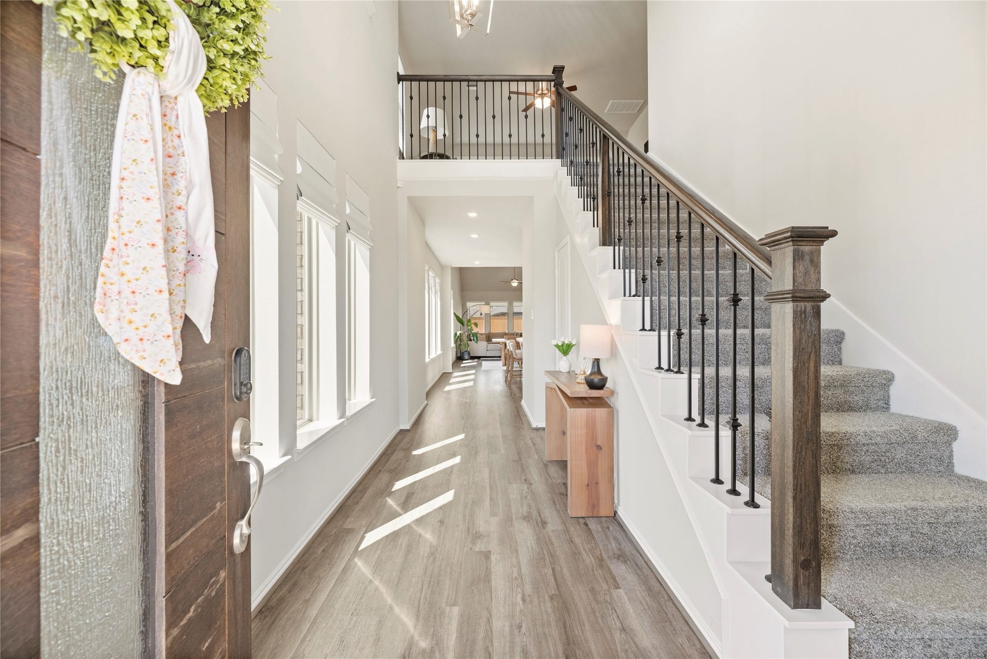 Bright and welcoming entryway with a modern staircase, warm luxury vinyl plank flooring, and ample natural light from large windows.