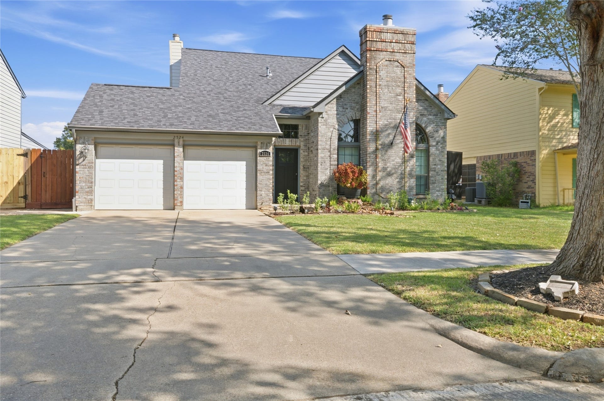 Charming two-story home featuring a brick faade, dual garage, and well-maintained front yard with mature trees and a welcoming pathway.