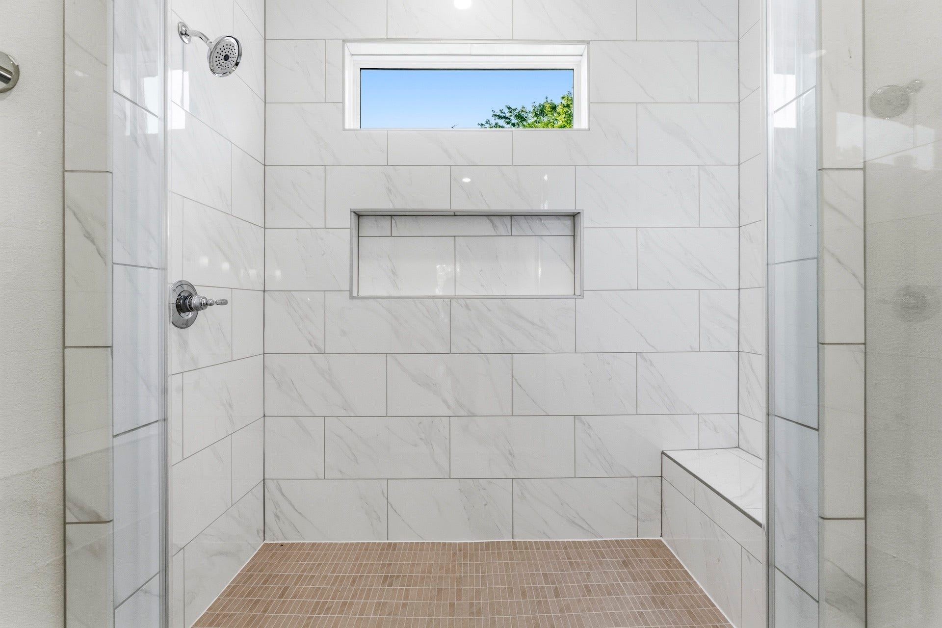 Thoughtfully Designed  This expansive primary shower, a comfortable seating bench, anchored
by a mosaic floor, floor to ceiling tiled surround, storage niche, all elegantly enclosed in
frameless glass.