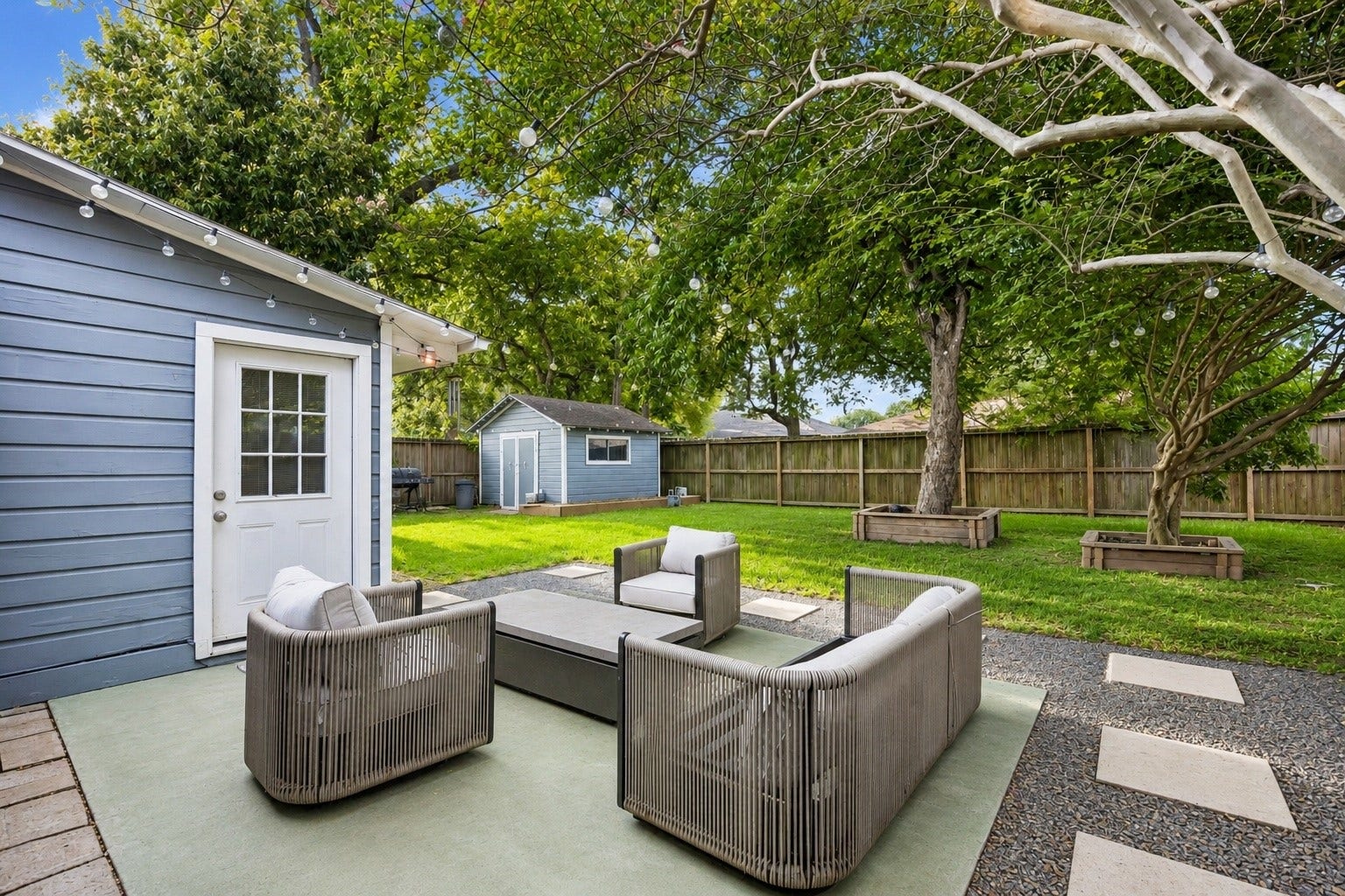 2214 Saxon Drive, Houston, TX 77018 Step outside to a patio designed for year round enjoyment, overlooking a beautifully maintained backyard shaded by mature trees. String lights, expansive green space, and a detached storage building create the perfect backdrop for outdoor entertaining, gardening, or weekend play.