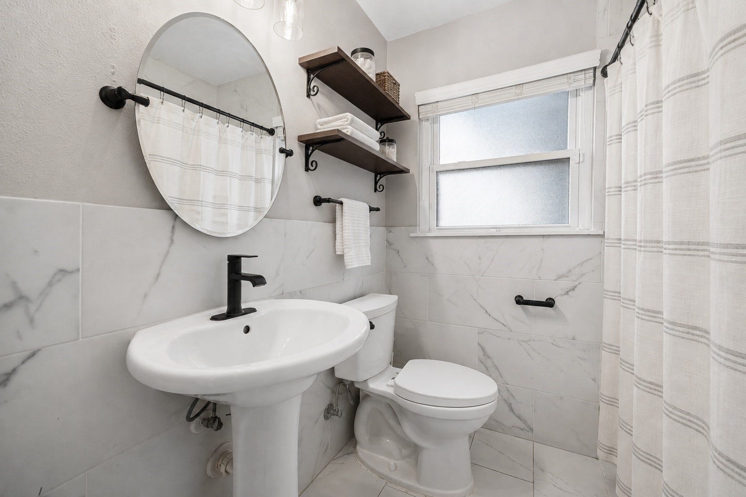 2214 Saxon Drive, Houston, TX 77018 Fresh finishes give this bathroom a bright, updated feel, featuring marble look tile, matte black fixtures, open wood shelving, and a clean, timeless design. Decorative styling adds warmth while maintaining a crisp, spa inspired aesthetic. **Virtually staged**
